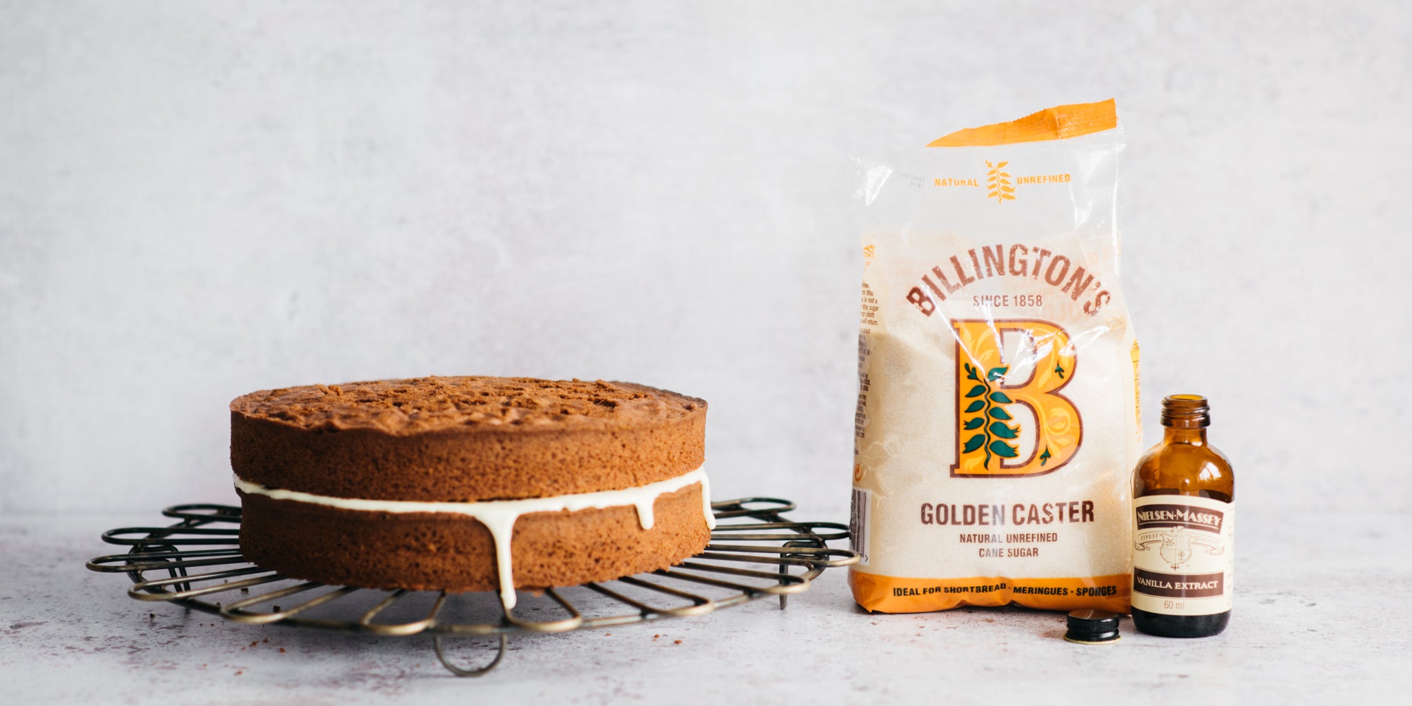 Cake on cooling rack next to bottle of vanilla and bag of sugar 