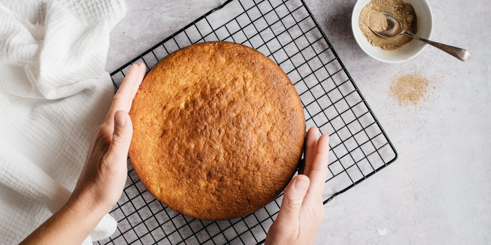 Hands touching a sponge cake on cooling rack