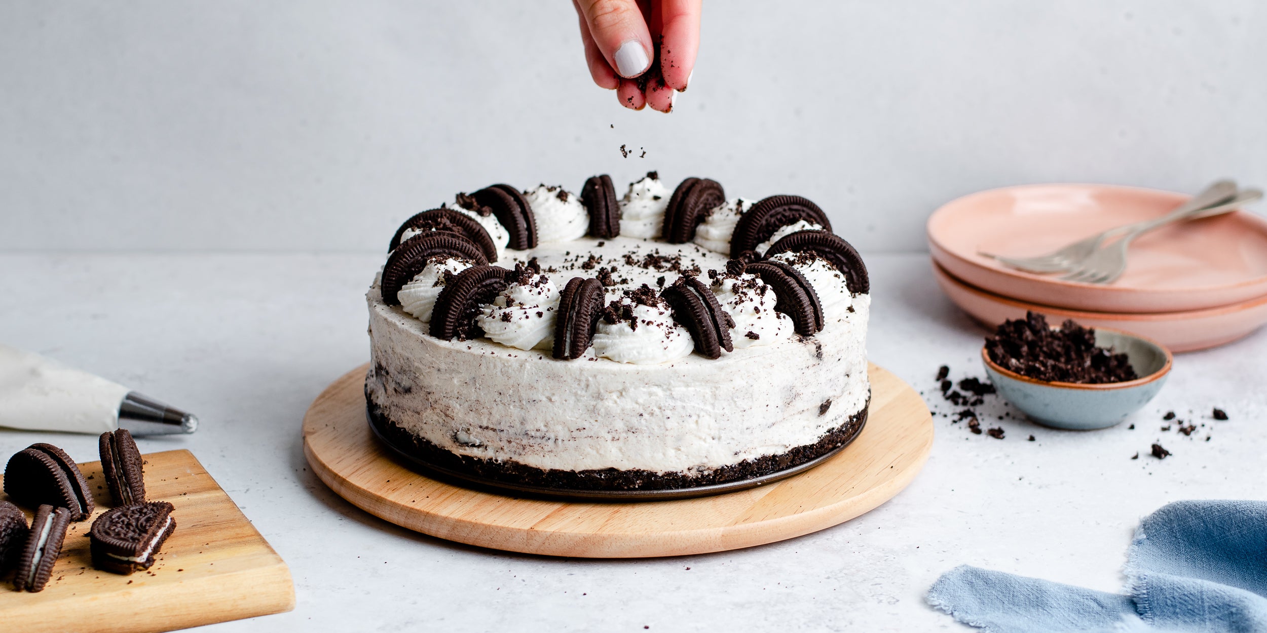 Oreo cookies being sprinkled on top of a no-bake Oreo cheesecake with cookies in the background