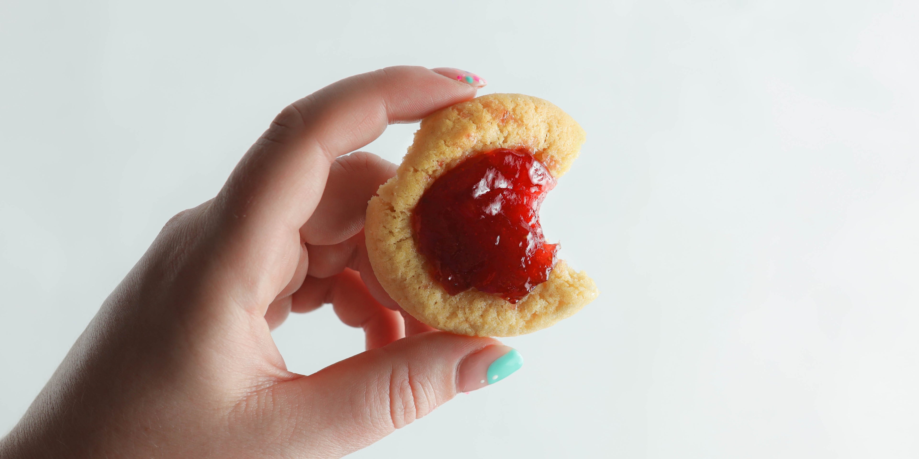 Hand holding biscuit with jam in it and a bite taken out