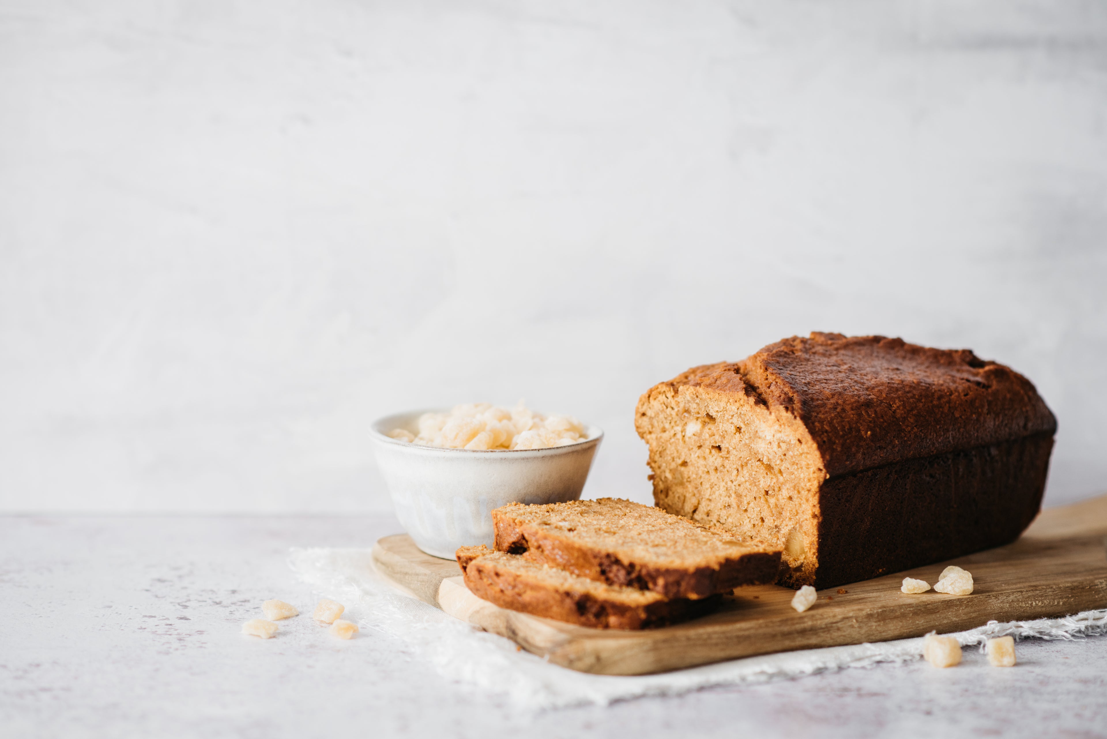 Gingerbread Loaf sliced on a wooden serving board, scattered with crystallised ginger