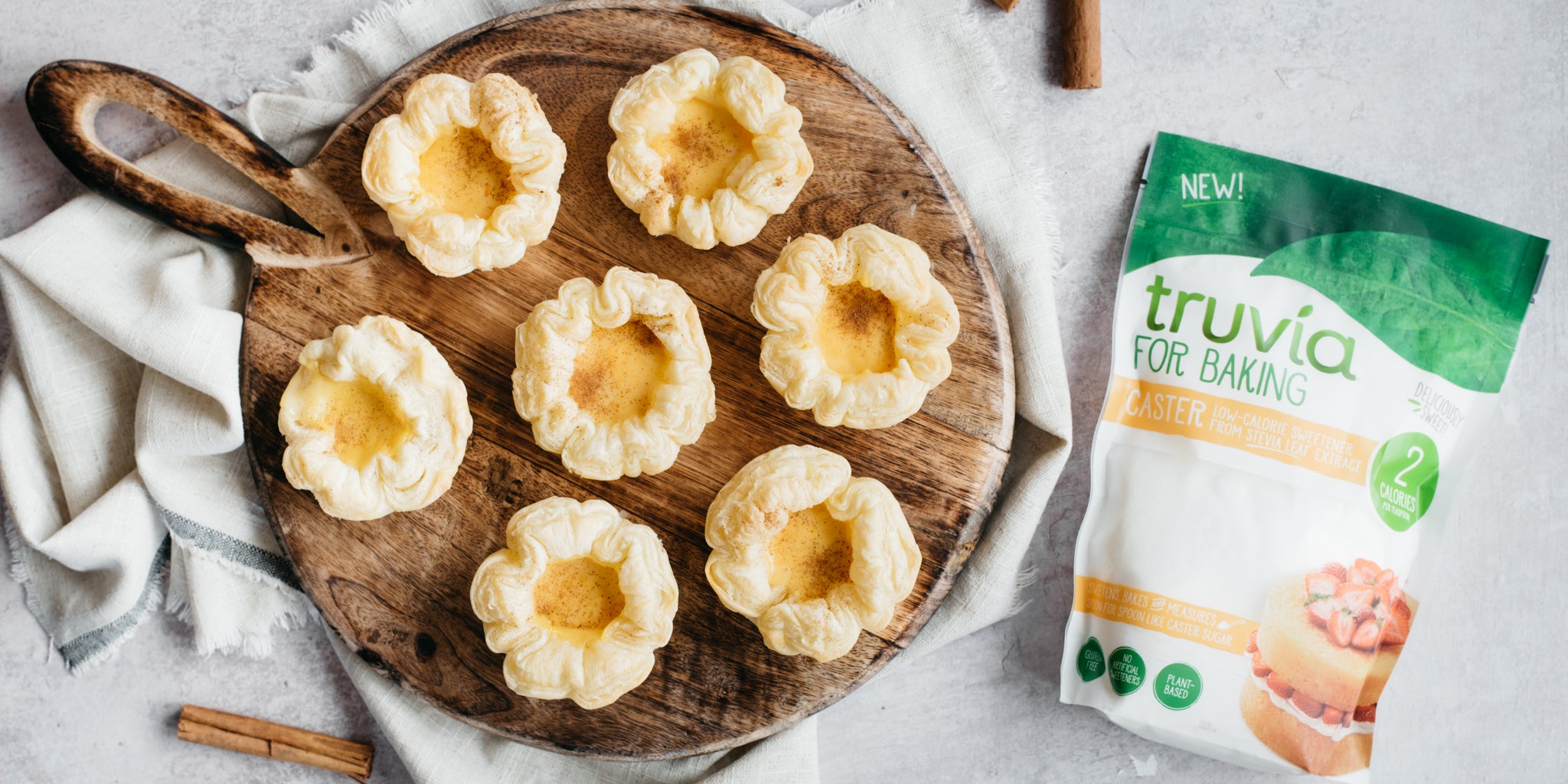 Circular wooden plate with 7 portuguese tarts on and a pack of sweetener beside