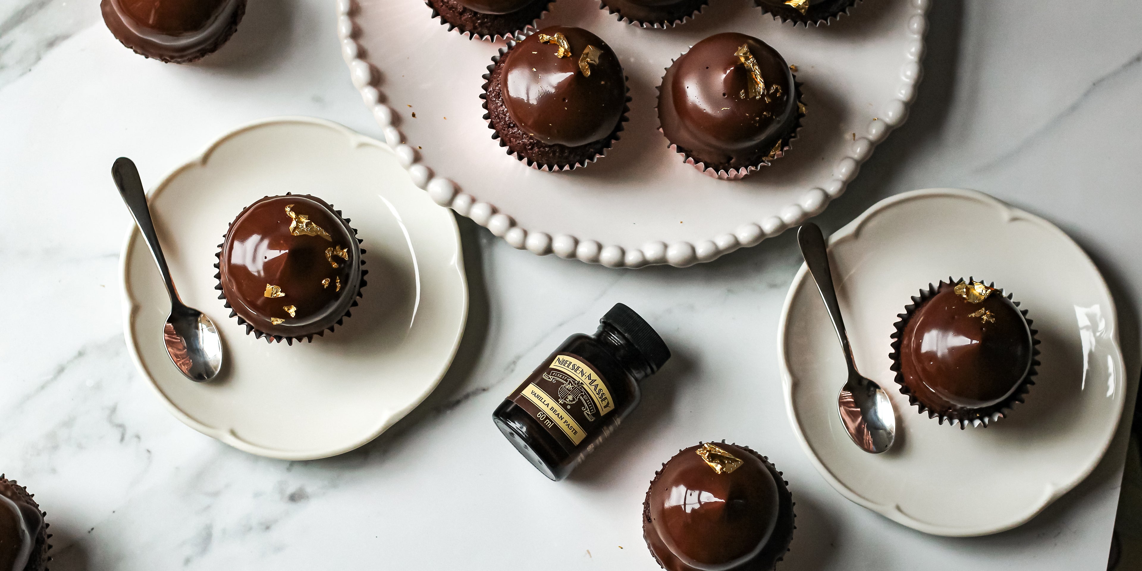 Top view of Hi-Hat Cupcakes on plates ready to serve, next to a bottle of Nielsen-Massey vanilla extract