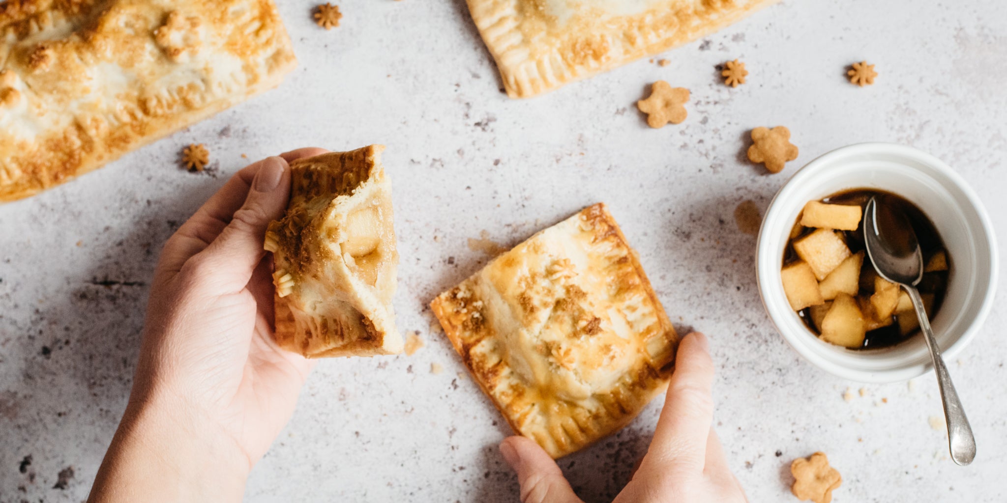 Hands pulling apart of an apple pie pocket with stewed apples beside it