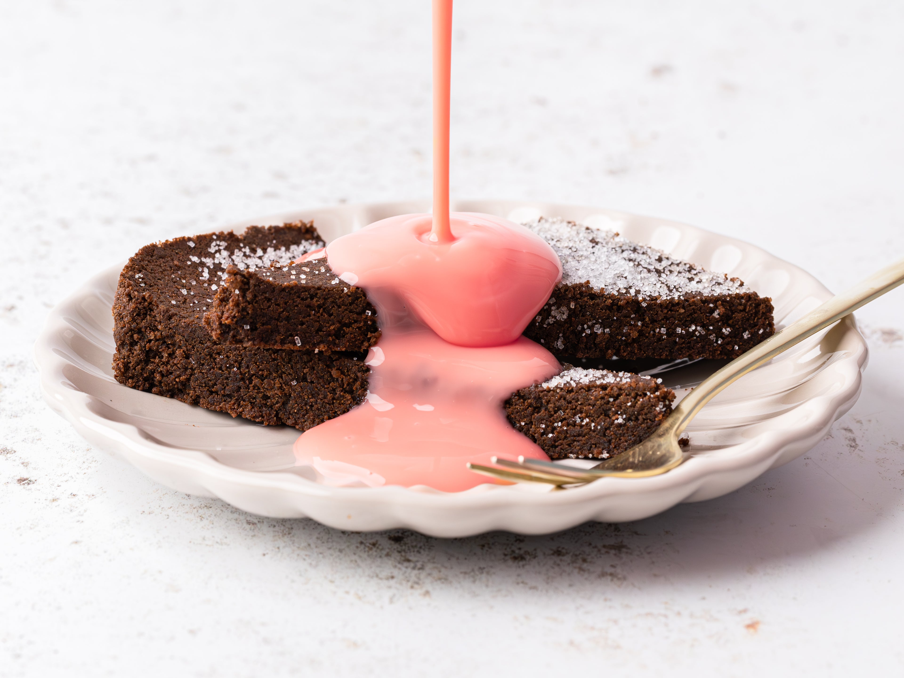 Chocolate concrete cake on a white plate topped with pink custard