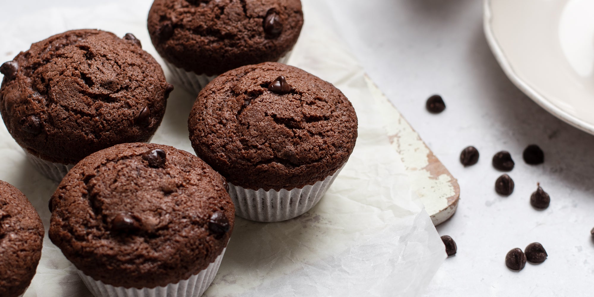 Close up of four Gluten Free Chocolate Muffins on a serving board next to scattered chocolate chips