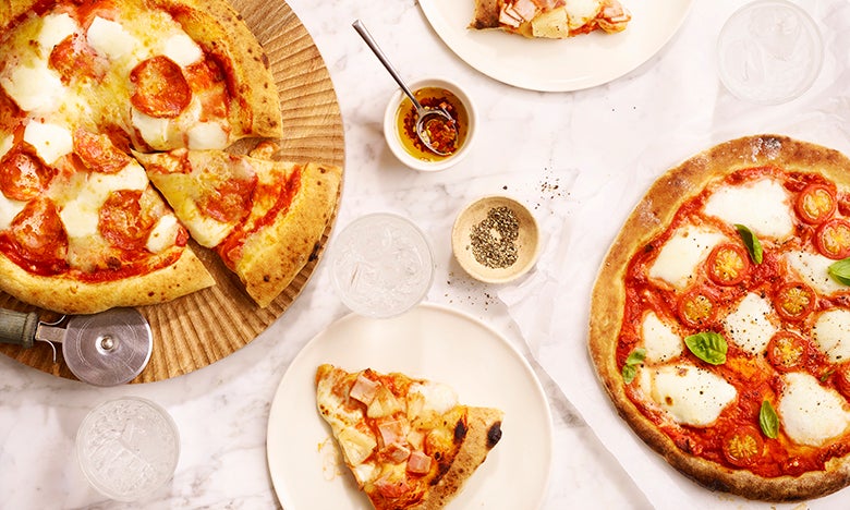 Two homemade pizzas made with fresh pizza dough on a white tabletop
