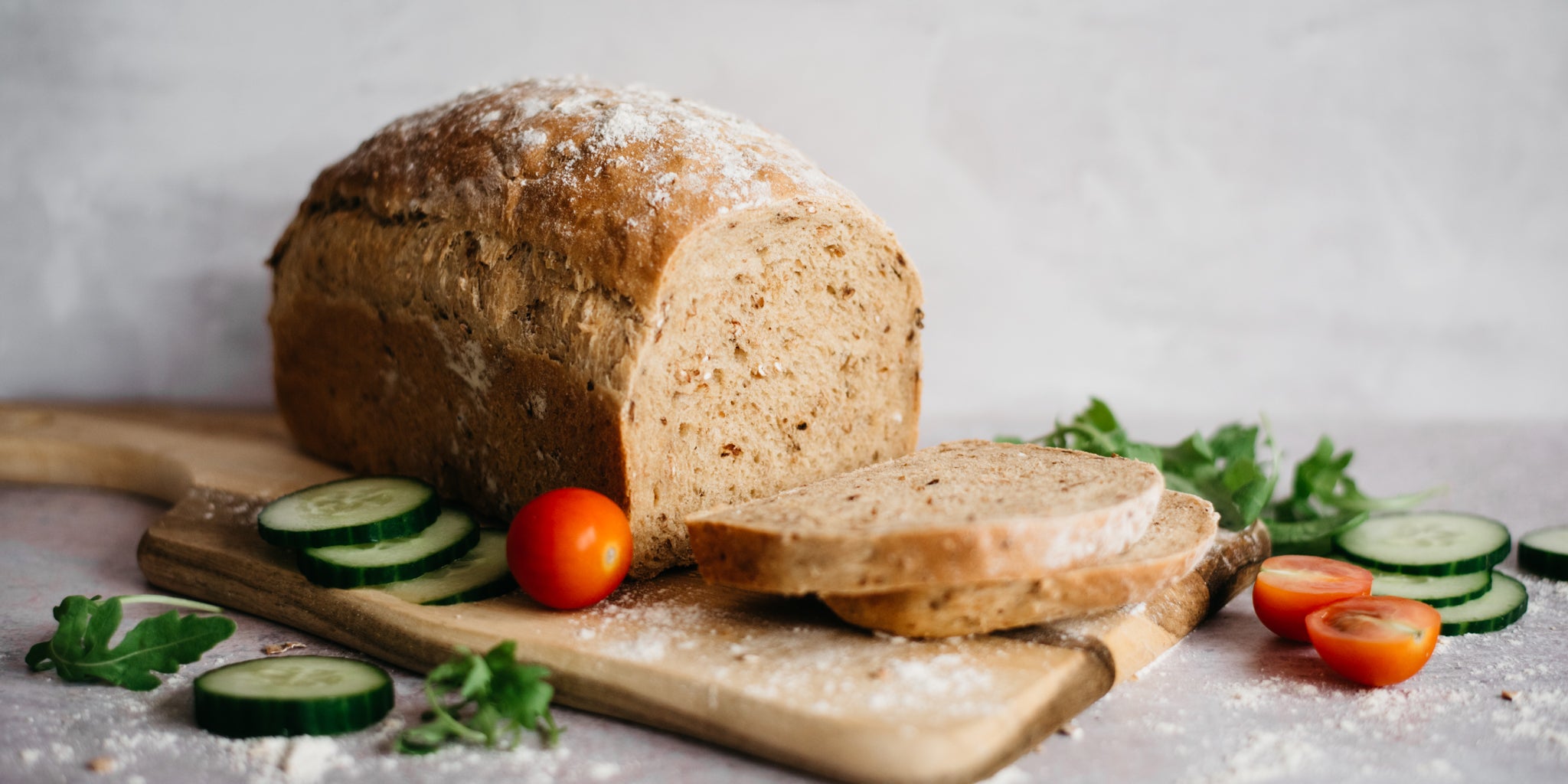 Farmhouse Country Grain Loaf sliced up on a serving board, with chopped salad garnished around it