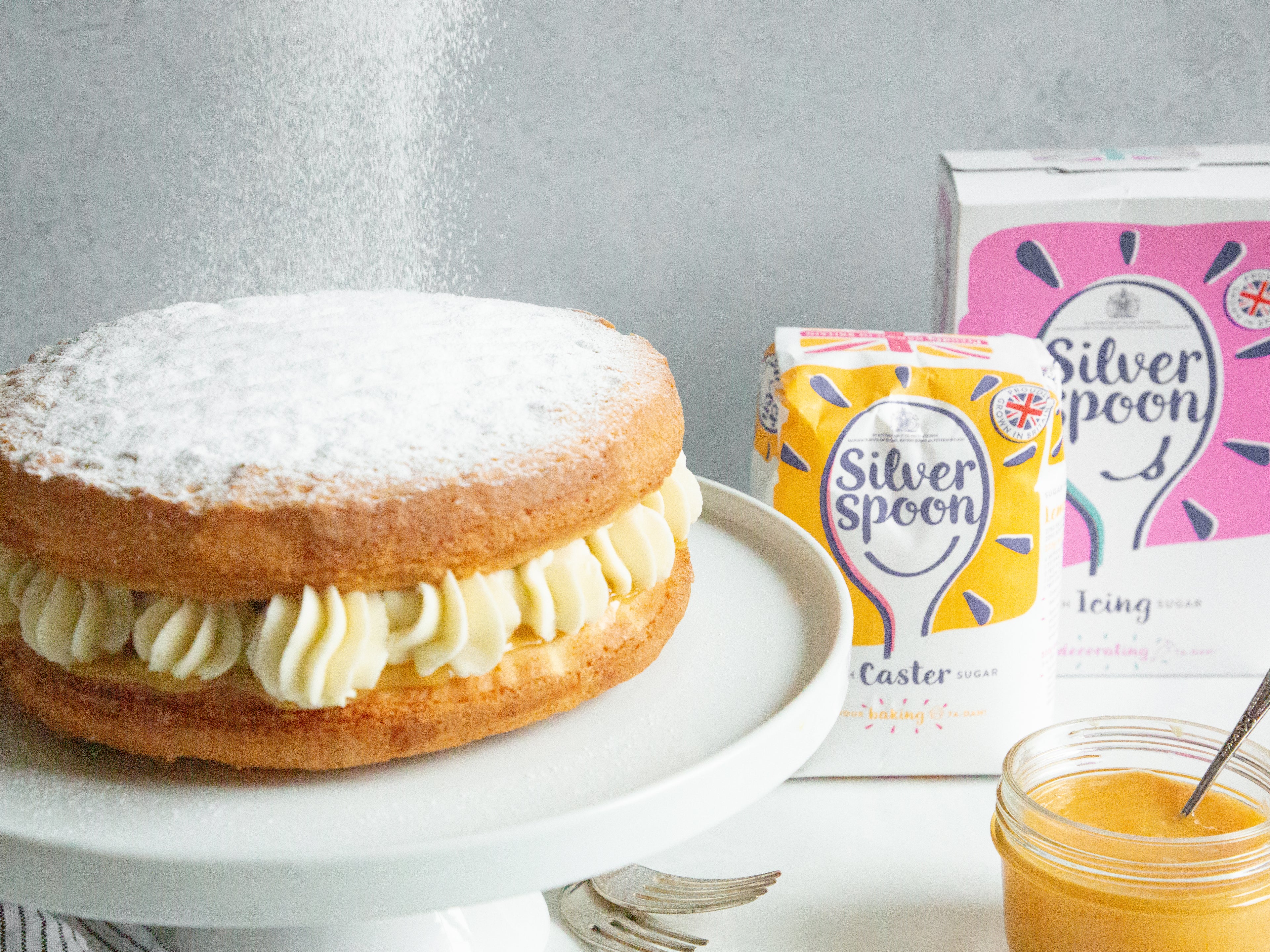Classic Lemon Cake dusted with Silver Spoon Icing Sugar, next to a box of Silver Spoon Caster Sugar and Icing Sugar