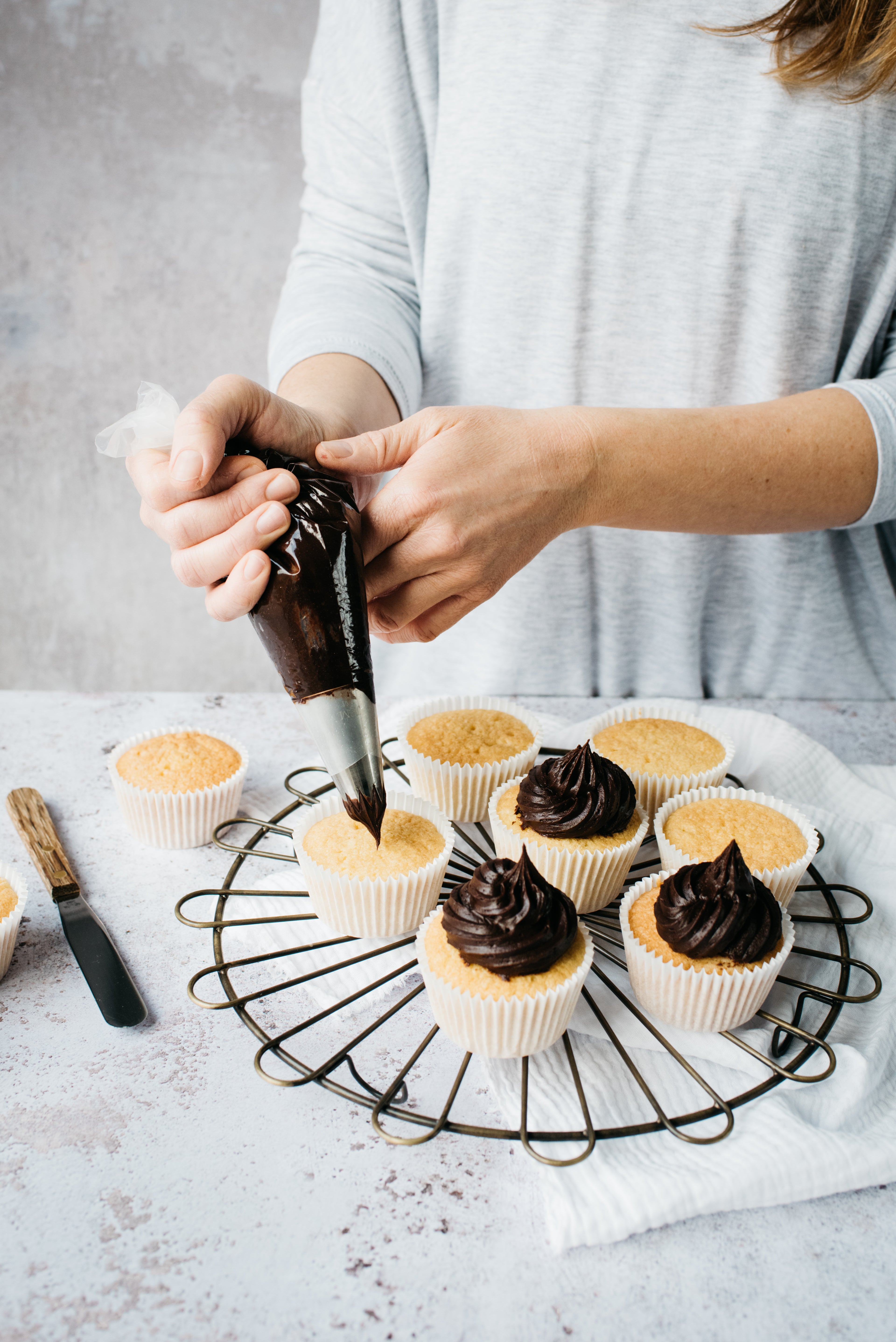 Baker piping chocolate buttercream on to a cupcake