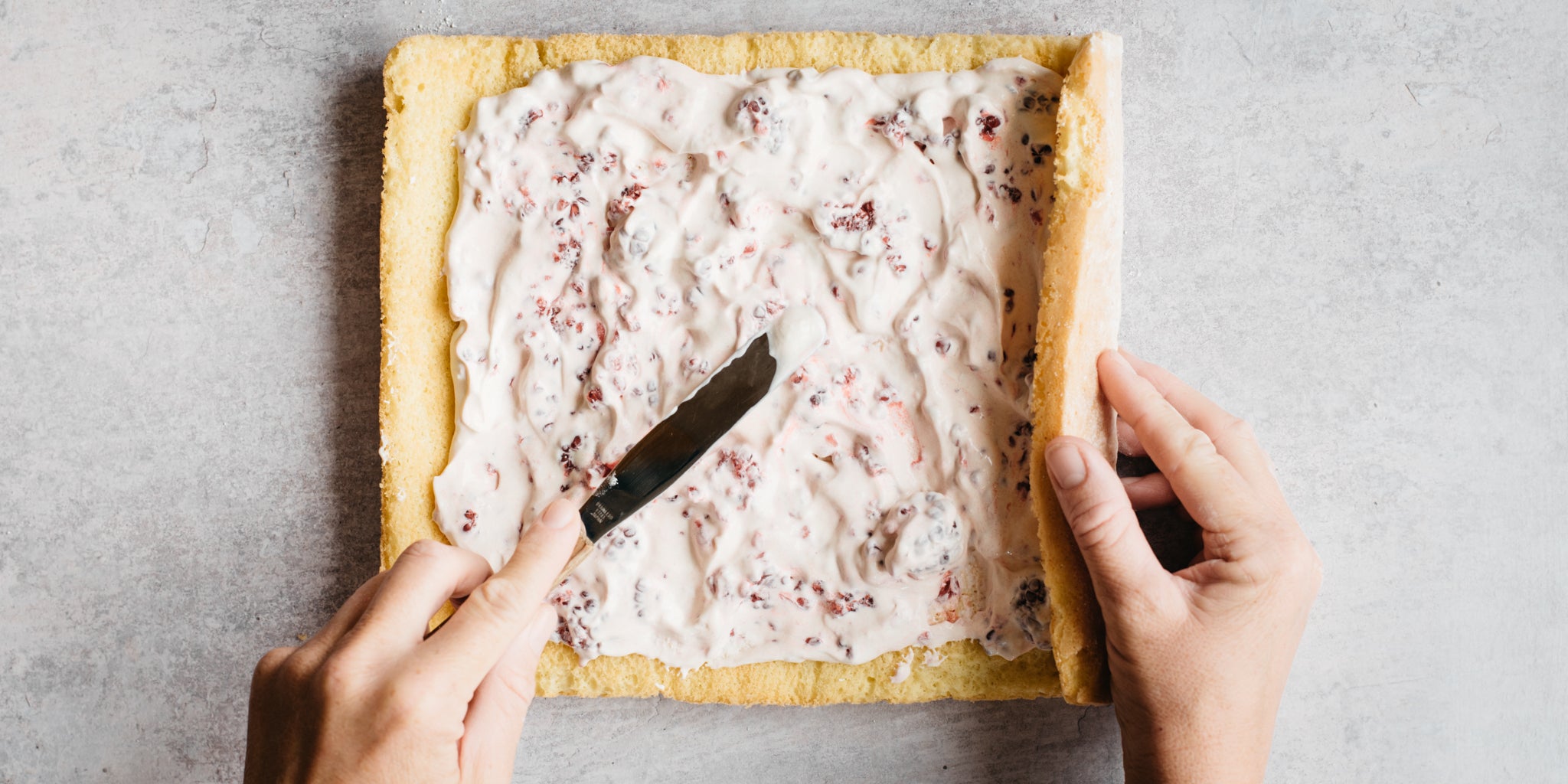 Creme fraiche and raspberries spread on top of sponge with a knife