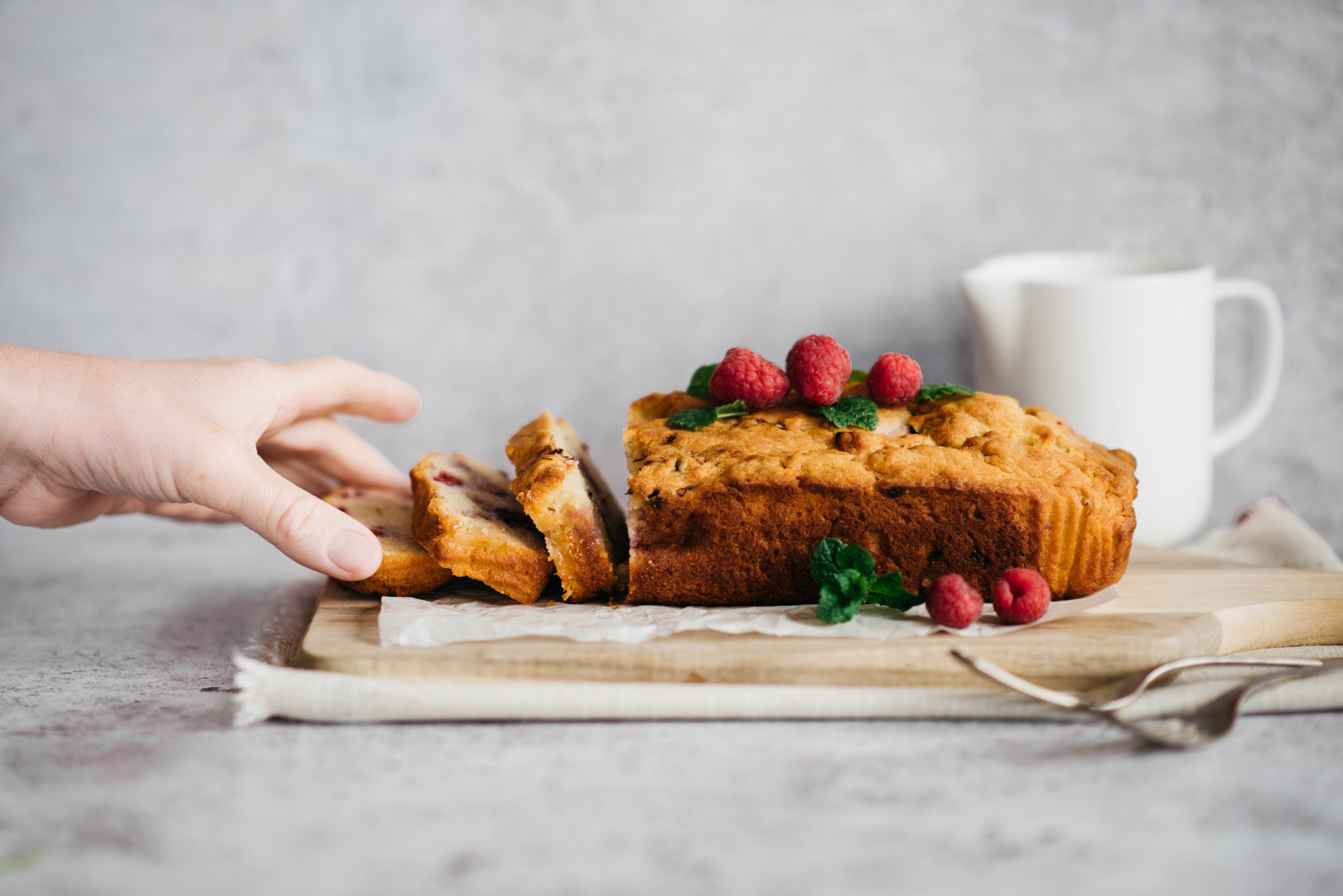 Raspberry & Mint Loaf Cake sliced into servings with a hand reaching for a slice