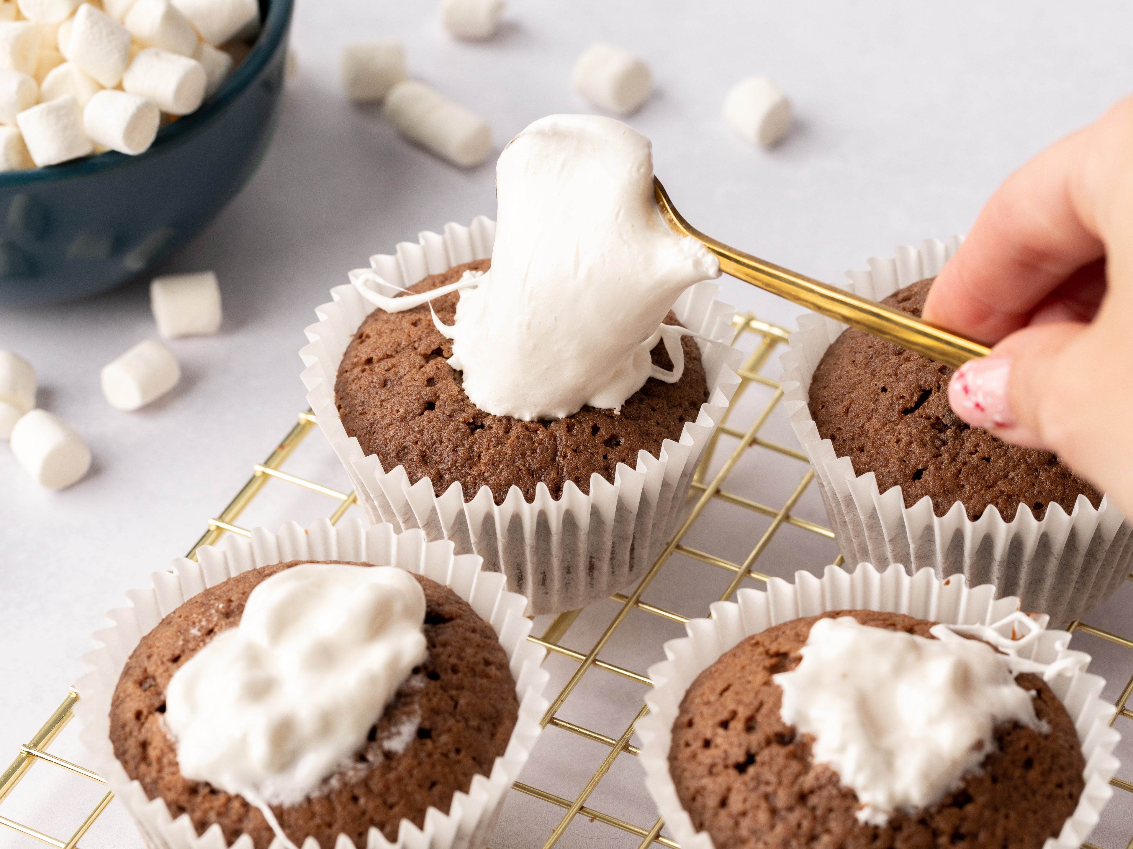 Hand spooning marshmallow into the center of chocolate cupcakes