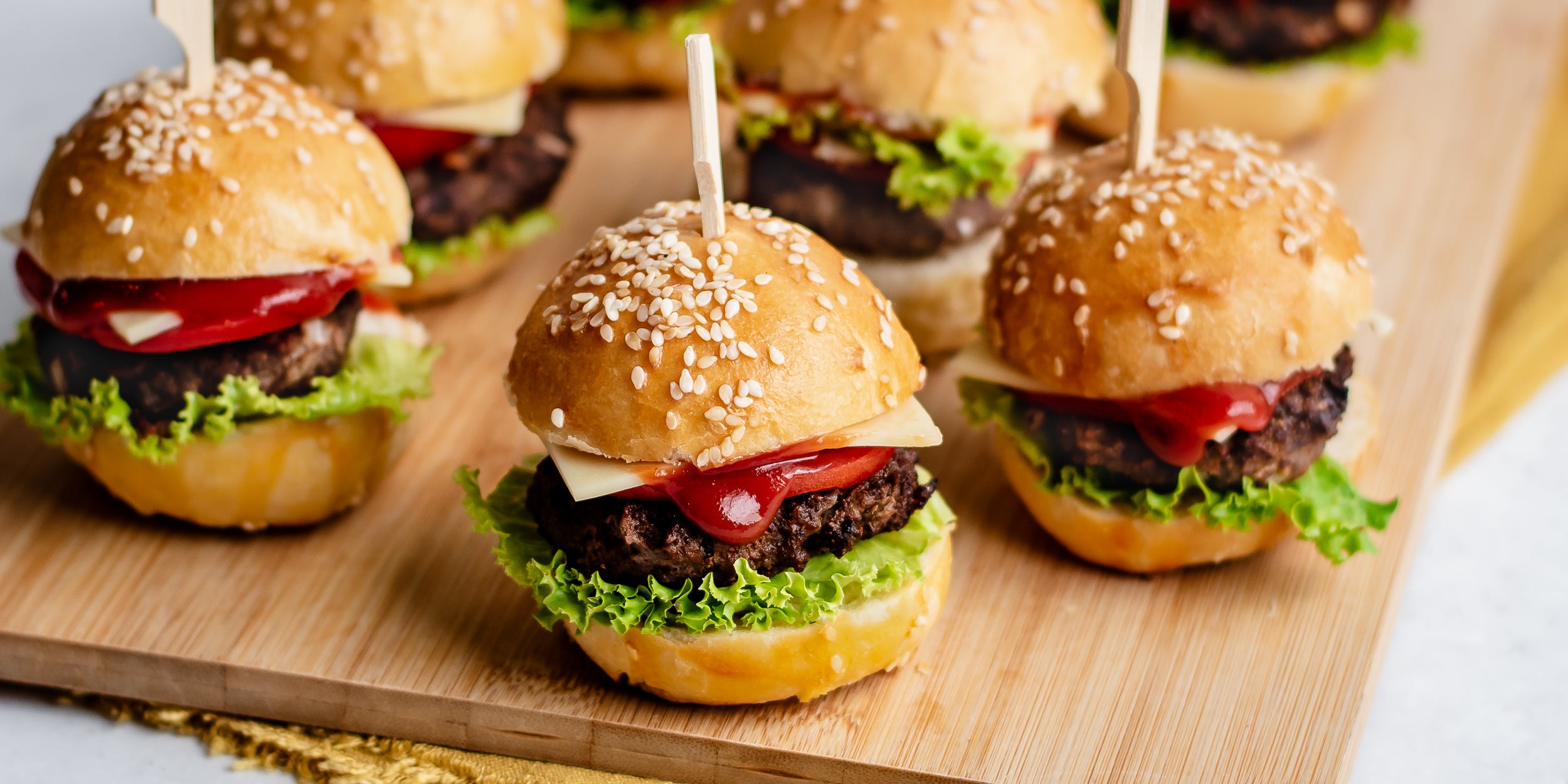 Close up of 3 mini burgers in buns with lettuce, cheese and tomato sauce
