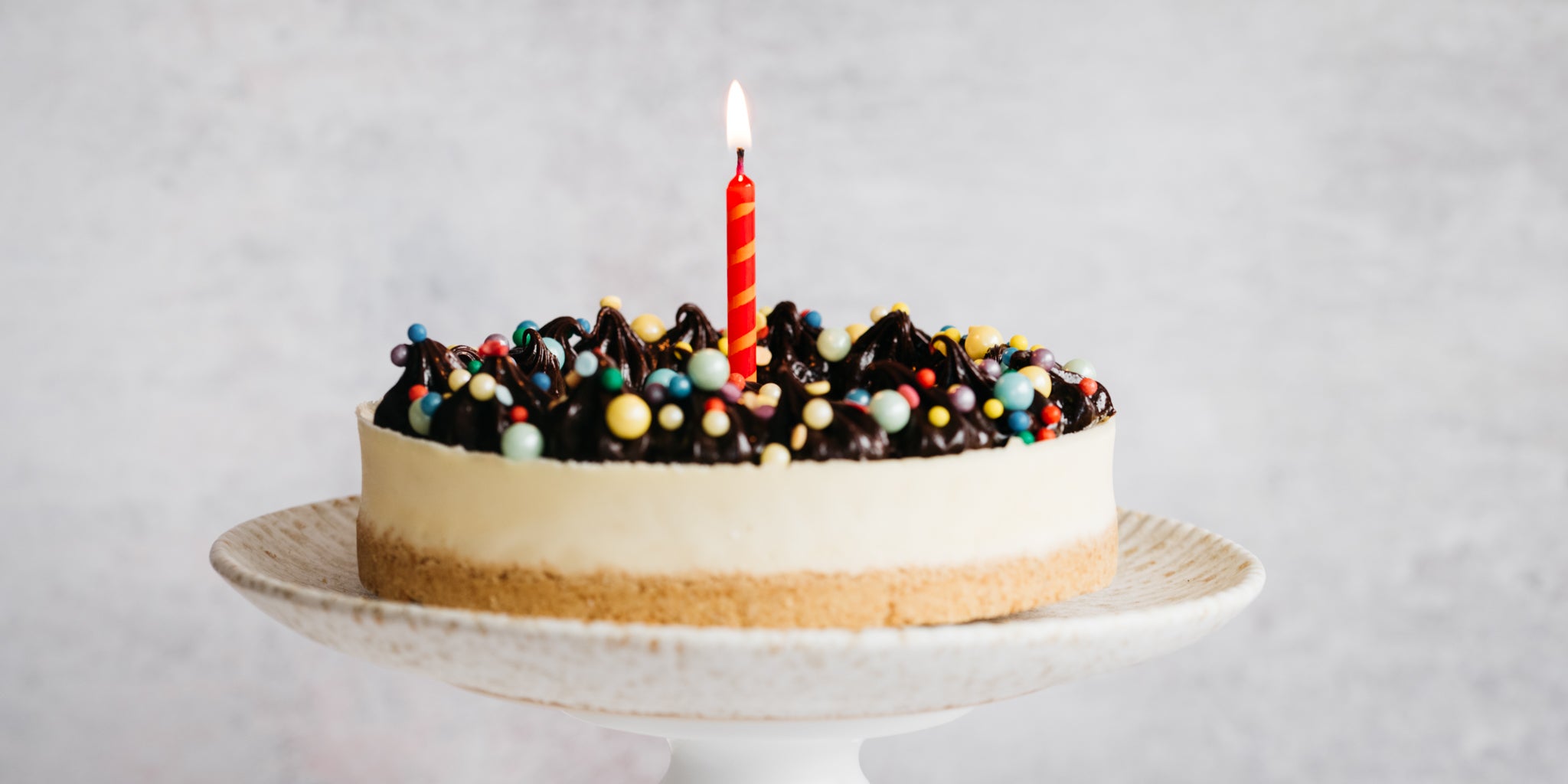 Cheesecake on a cake stand decorated with sprinkles and a lit red candle