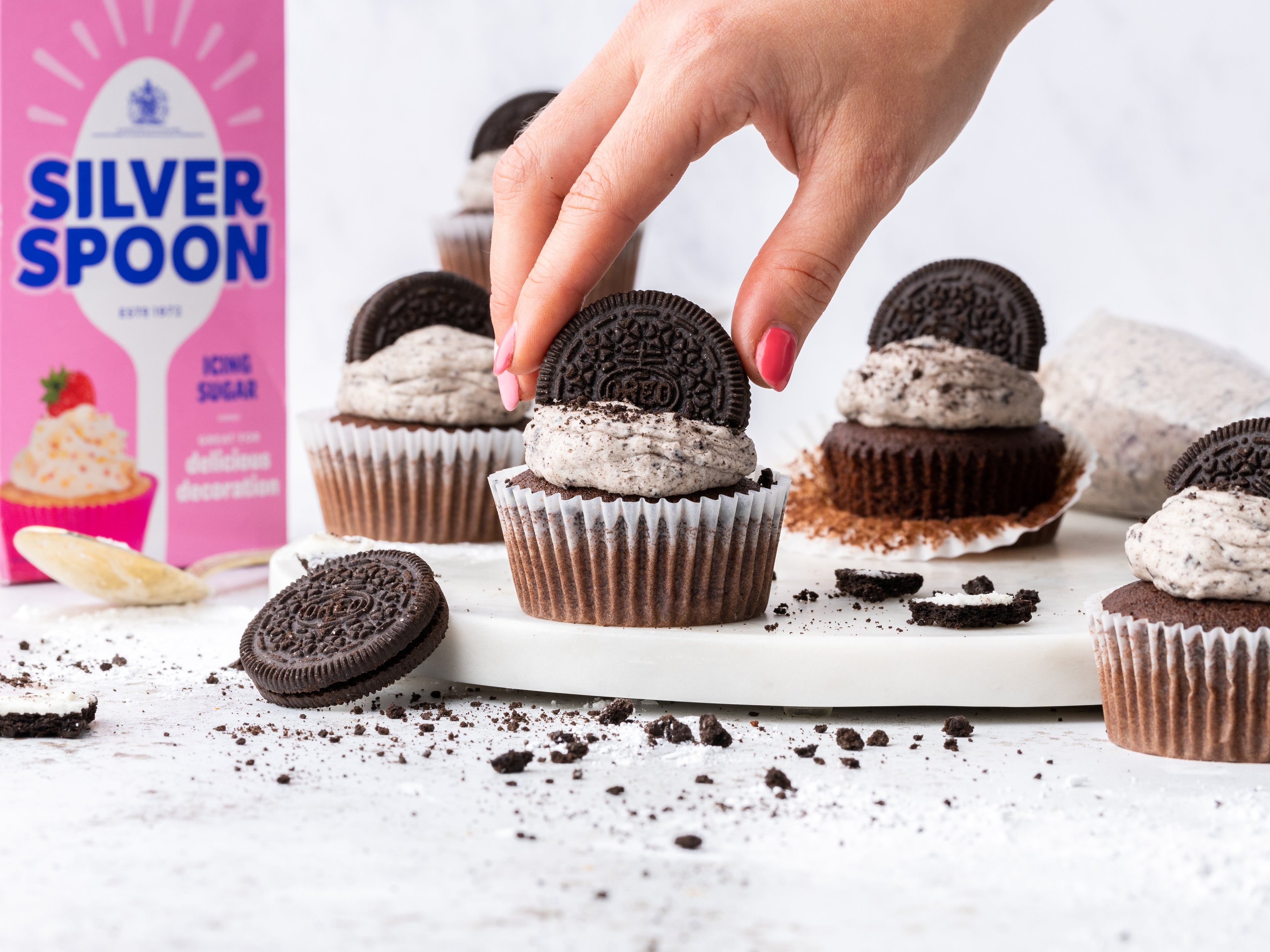 Hand reaching in to place an oreo on top of a cupcake
