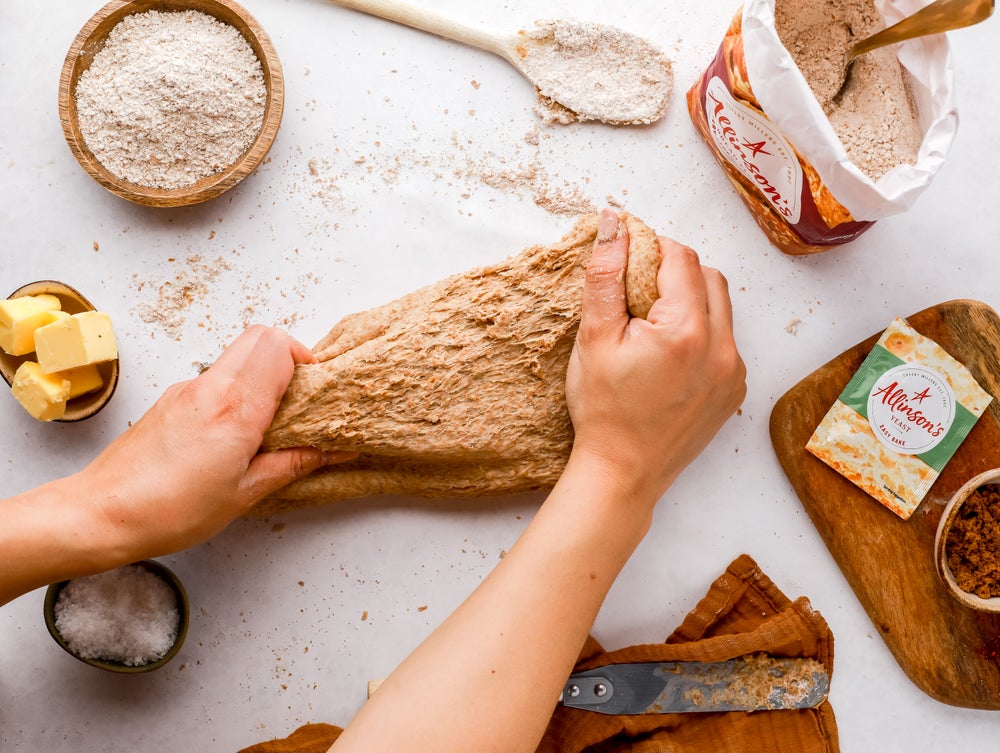 Hands kneading dough beside yeast packet