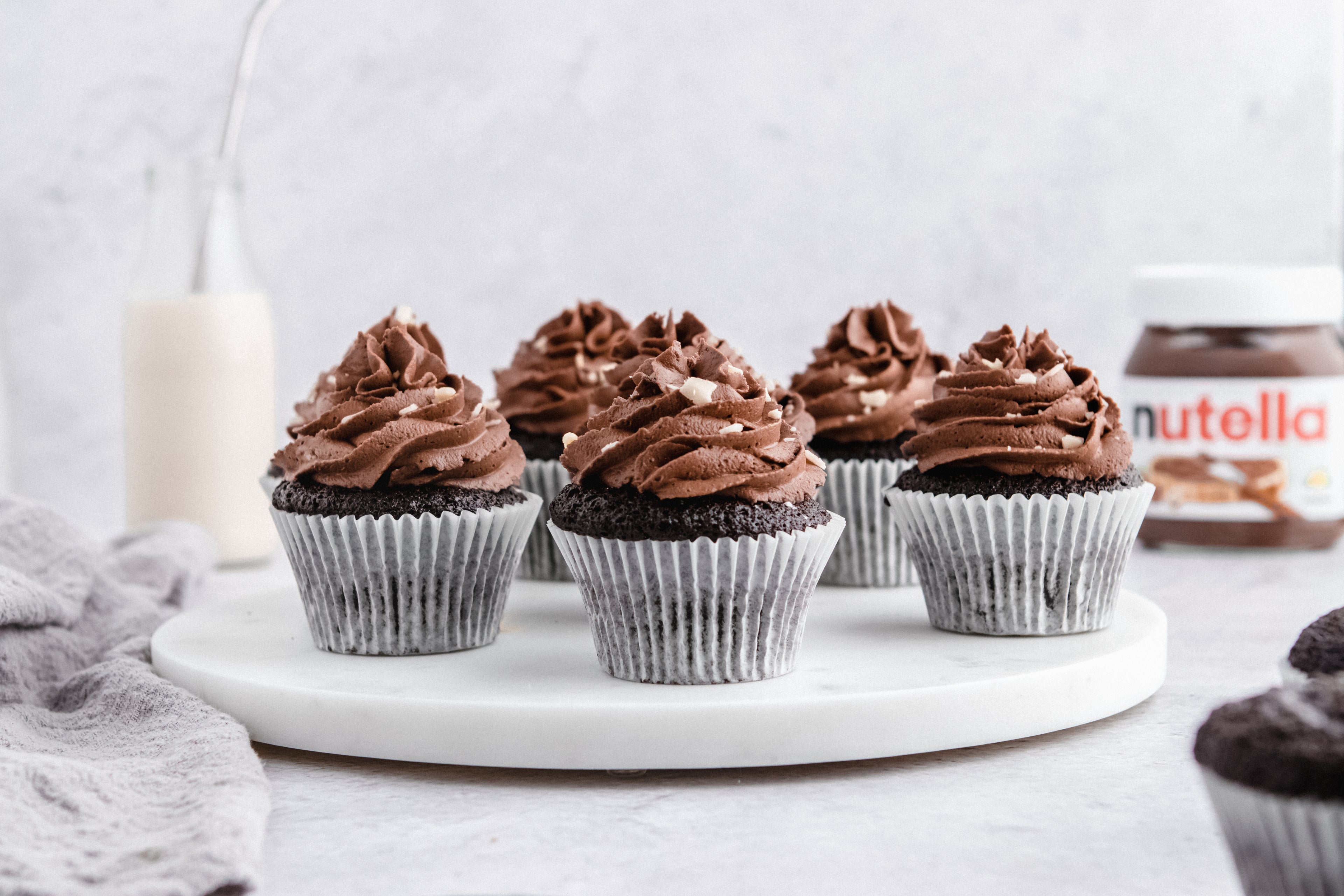 Nutella Cupcakes on a marble board, with a bottle of milk and jar of Nutella in the background