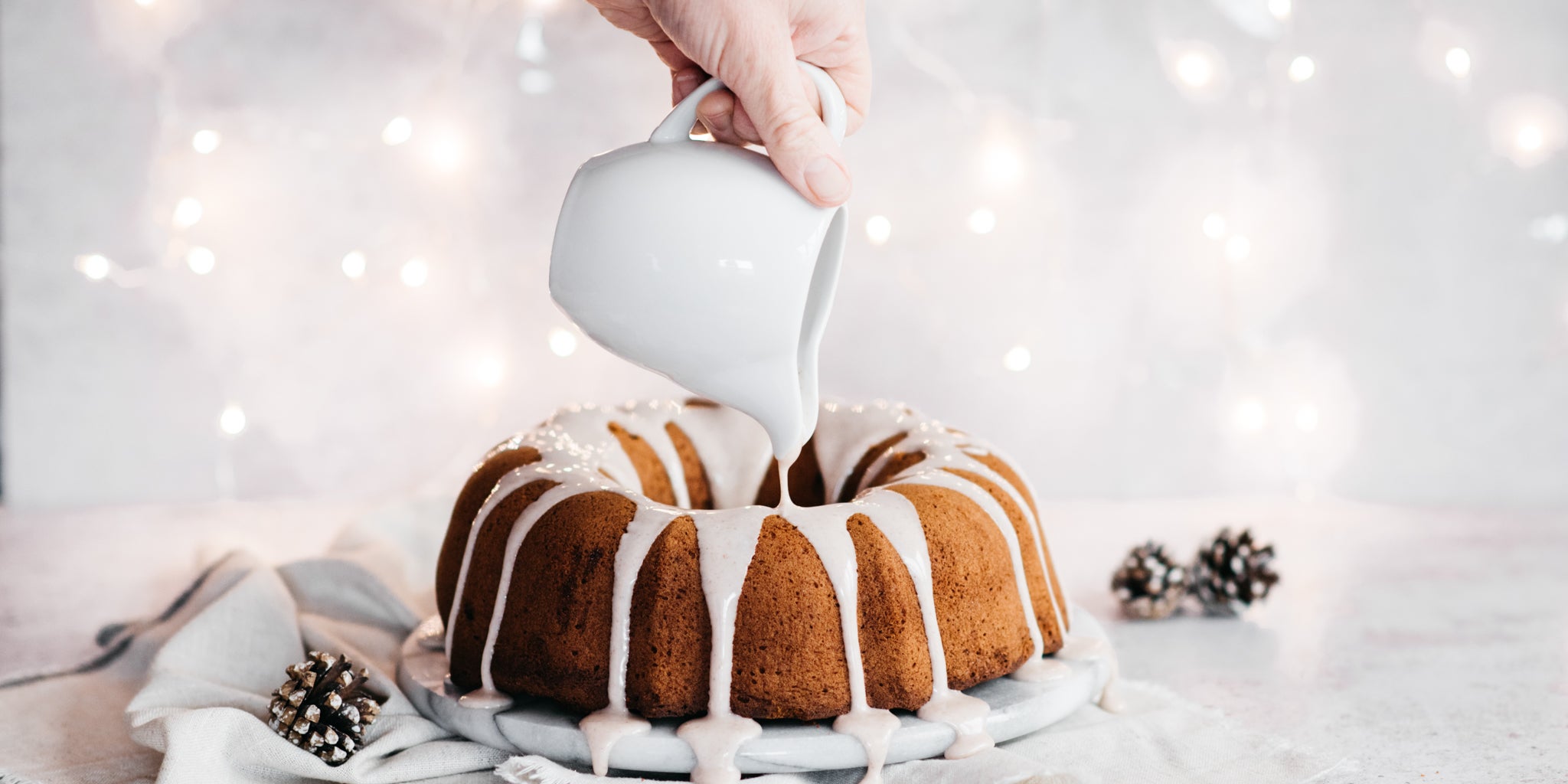 Hand pouring icing from a jug over the top of the gingerbread bundt cake