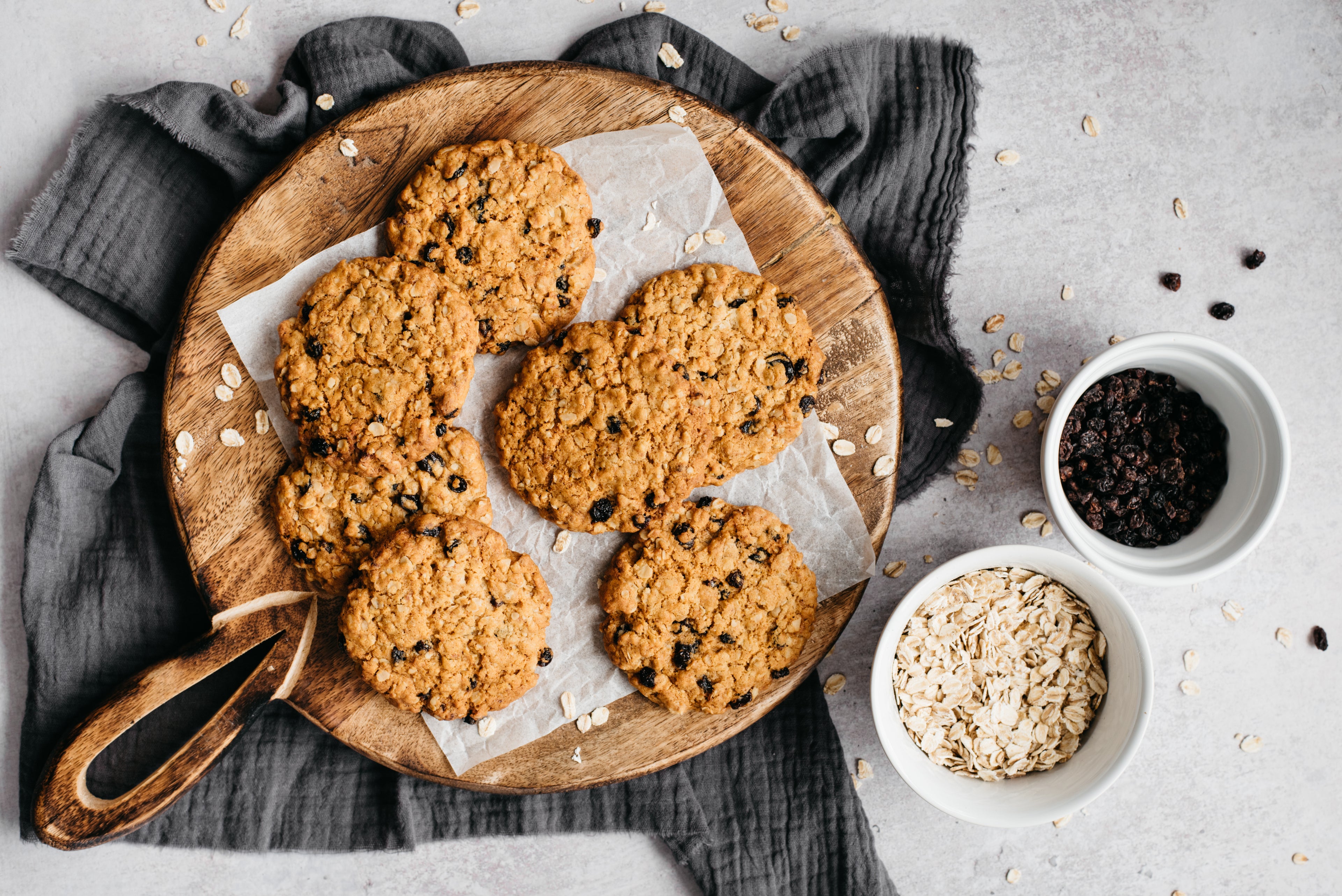 Top view of a batch of Oat & Raisin Cookies next to a bowl of oats and raisins