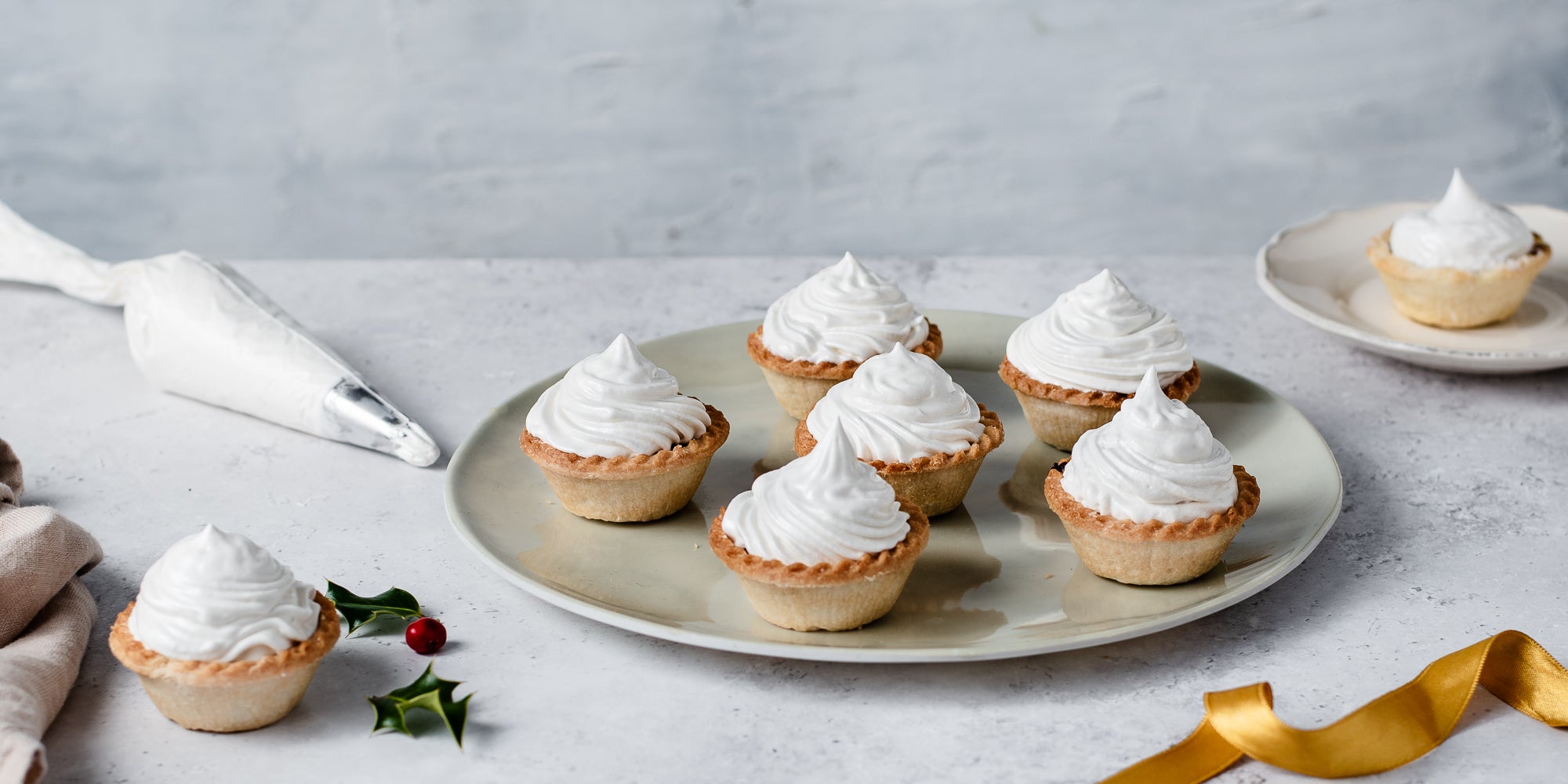 Meringue Topped Mince Pies on a serving plate next to a piping bag of meringue