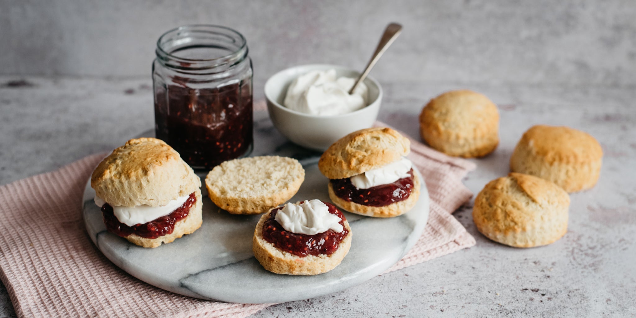 Close up of Vegan Scones on a serving board, sliced in half with jam and plant based whipped cream