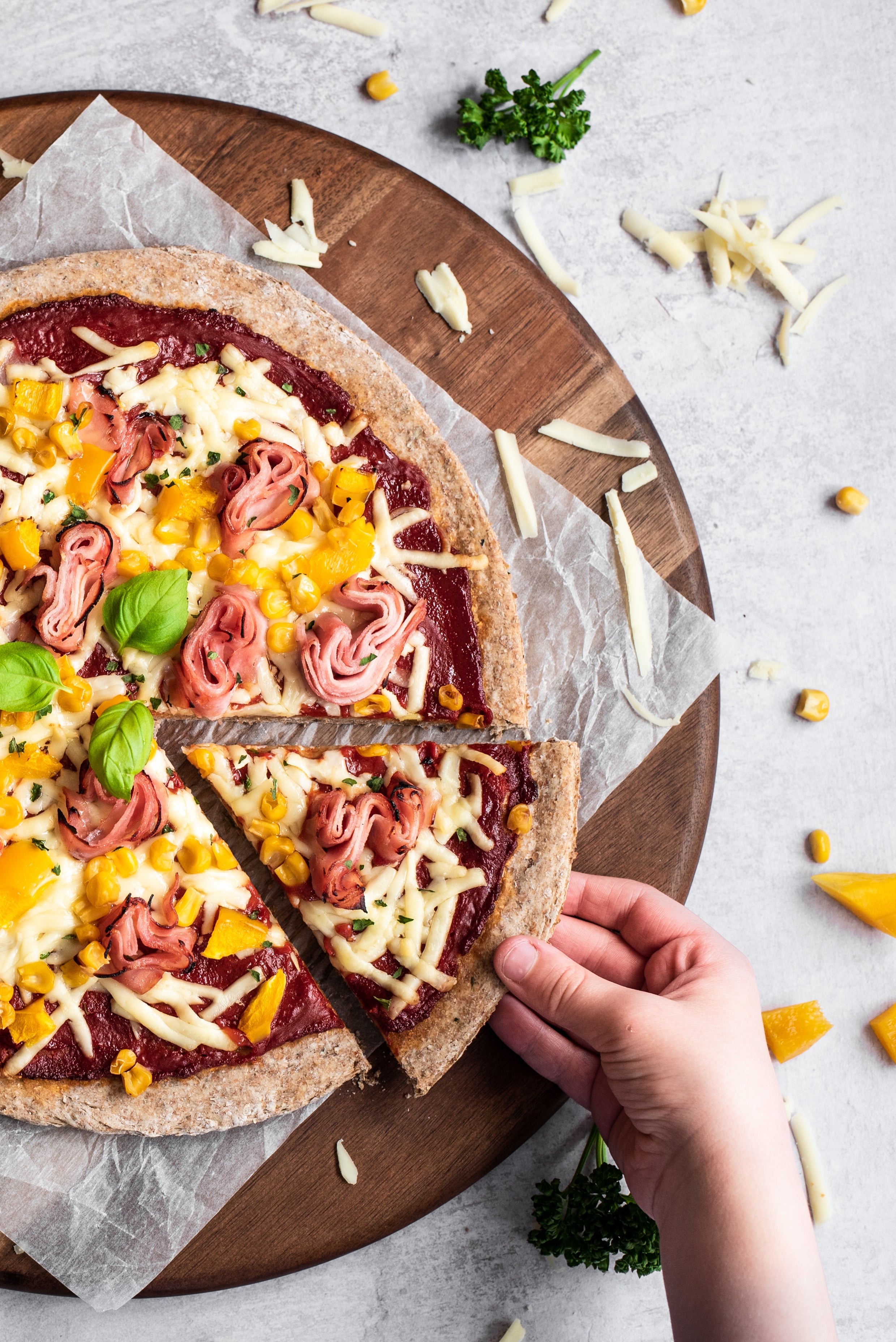 Close up of ham and pineapple pizza with hand reaching in removing a slice