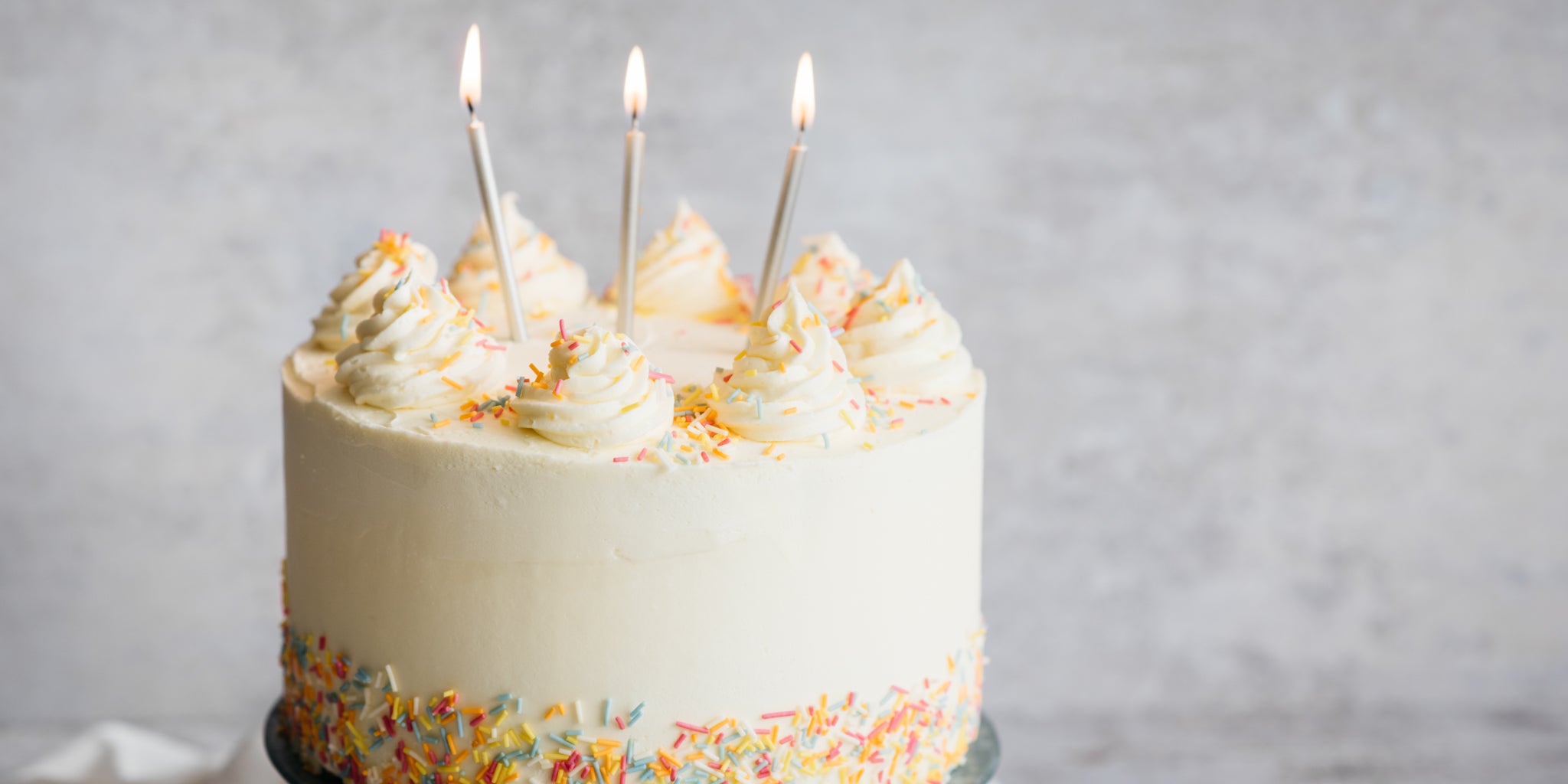 Close up of Vegan Vanilla Cake topped with Vanilla Icing Swirls, and candles stuck into the top, lit for a Birthday