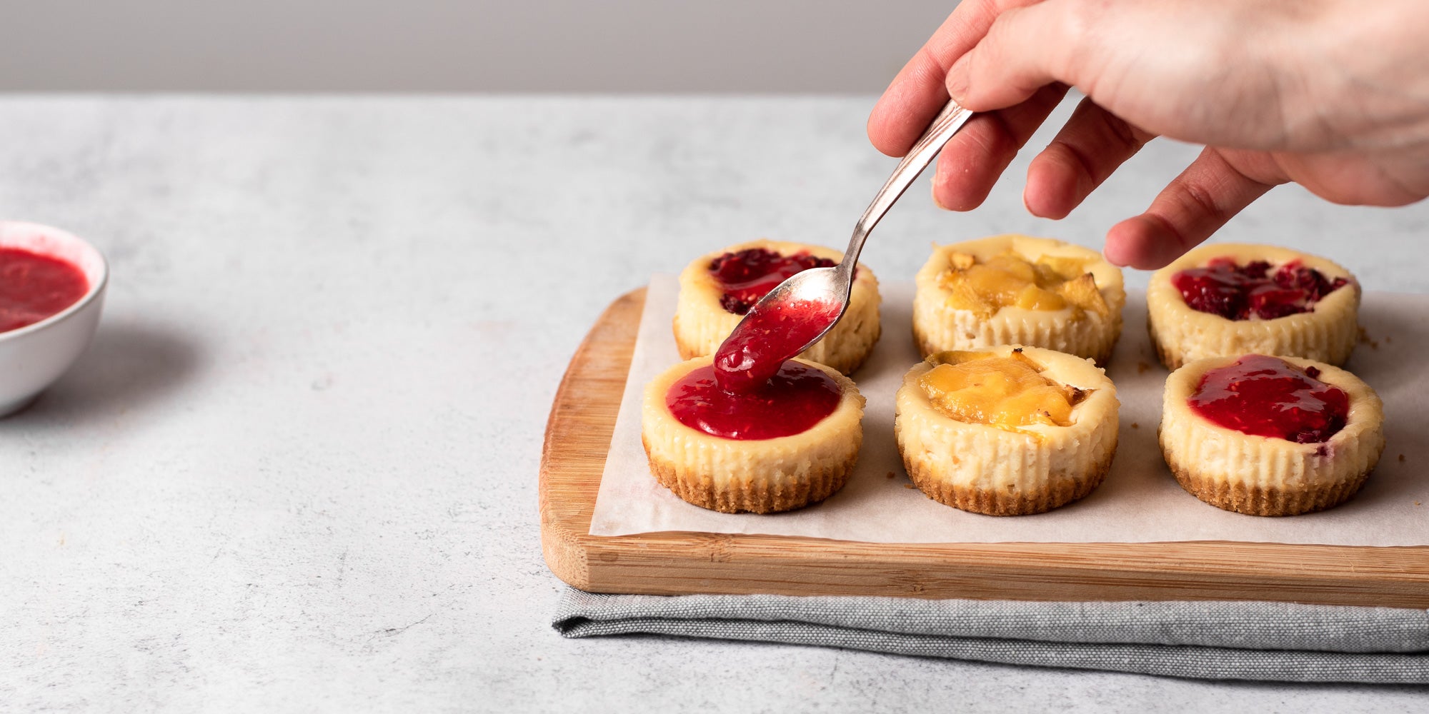 person putting raspberries on mini cheesecakes with a spoon