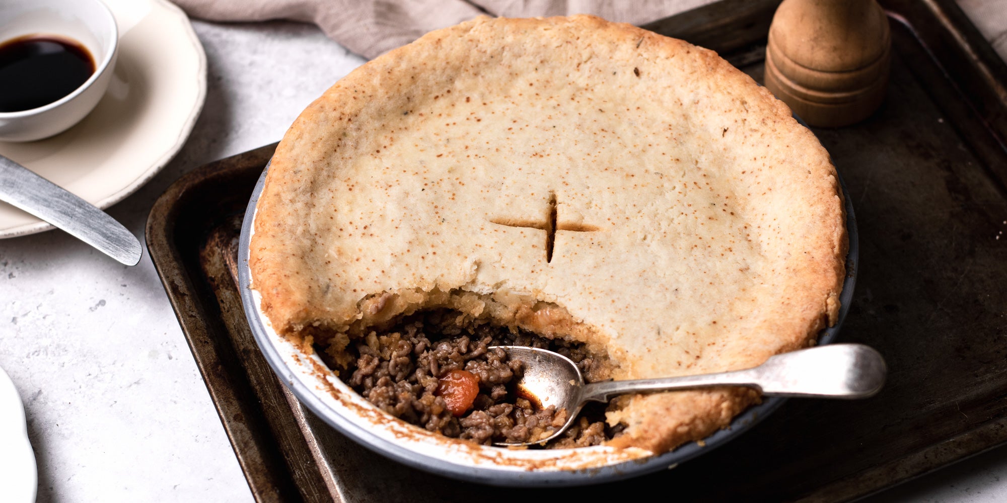 Close up of Suet Crusted Beef & Onion Pie, with a spoon inside the filling. Served on a baking tray