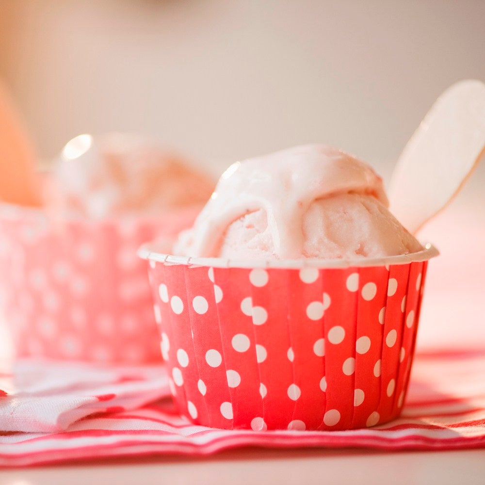 Scoops of homemade strawberry ice cream in a polka-dot cardboard tub