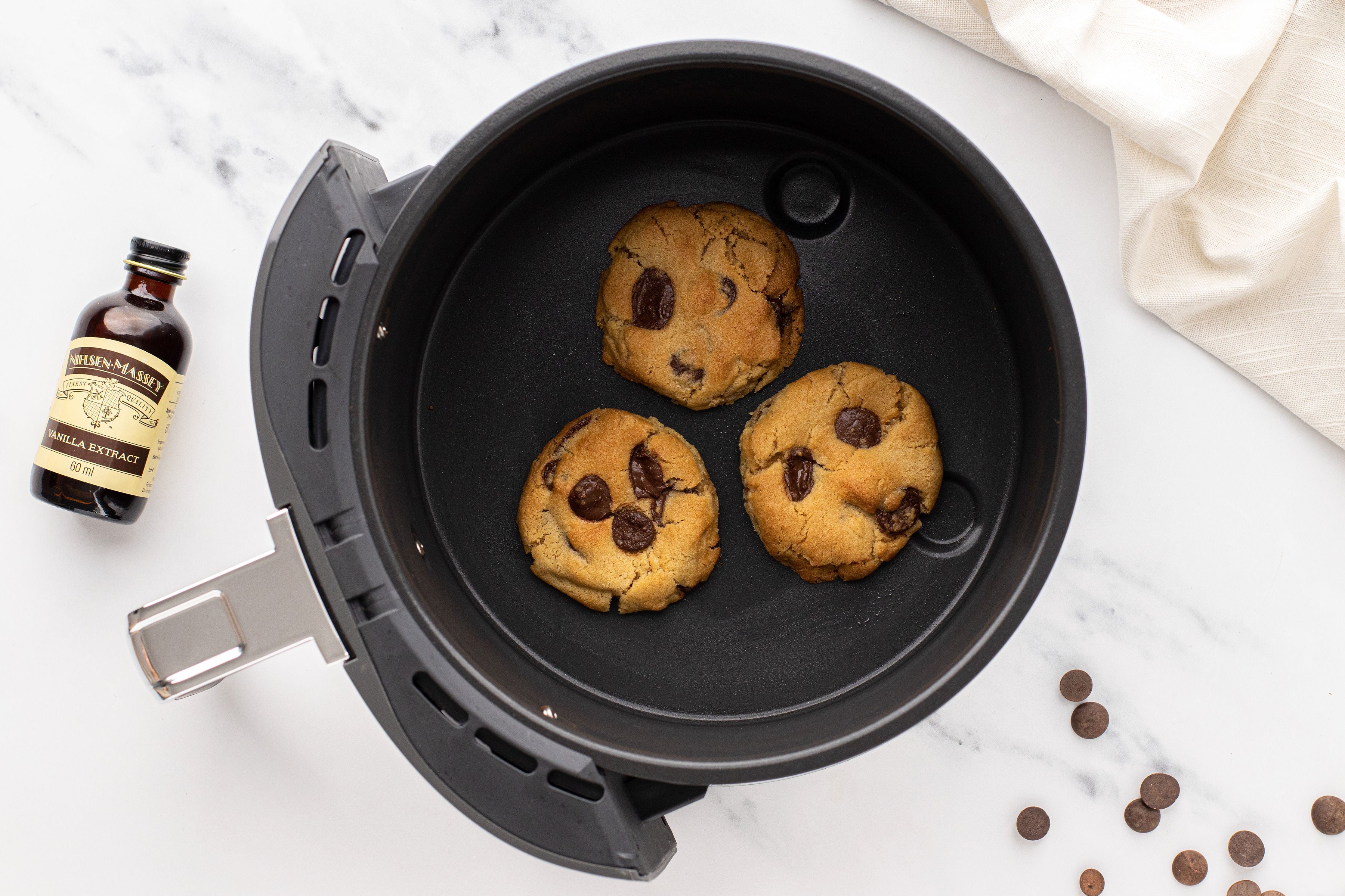 Top view of Air fryer Copycat Millie's Cookies in an air fryer next to a bottle of Nielsen Massey