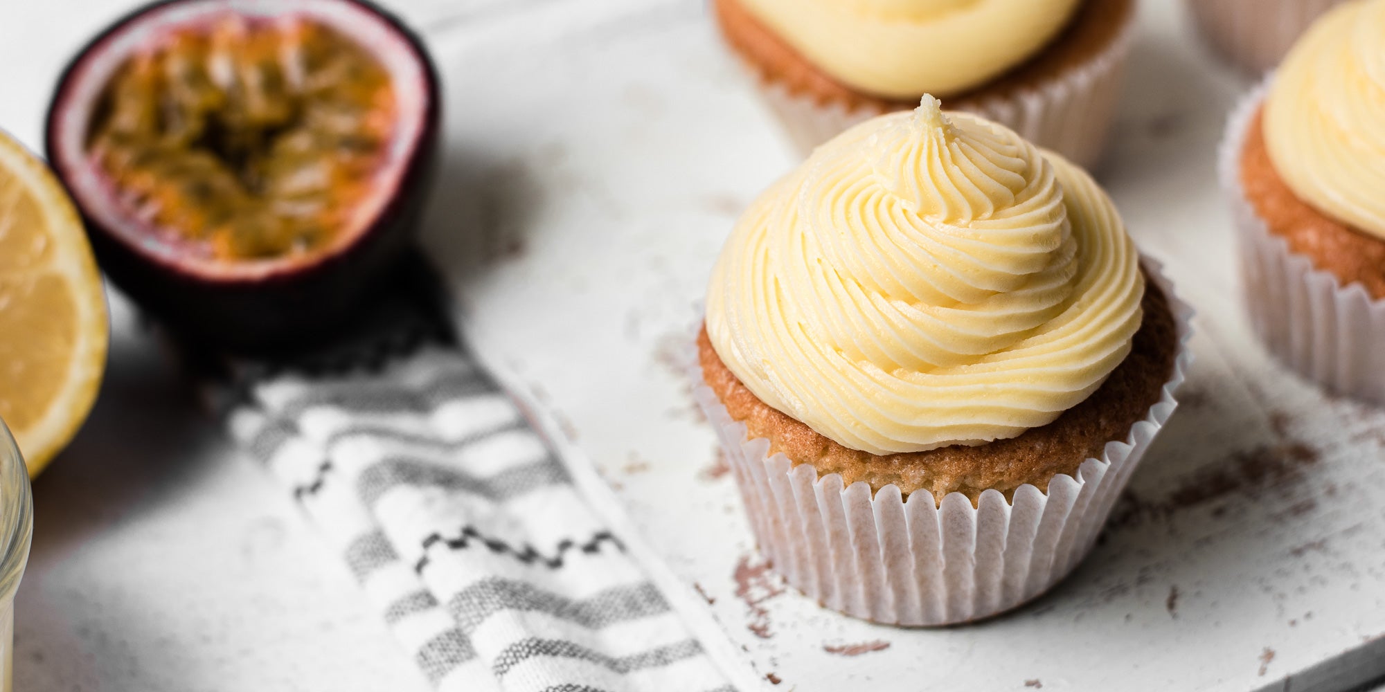Cupcakes topped with passion fruit Icing next to a slice of passion fruit and lemon