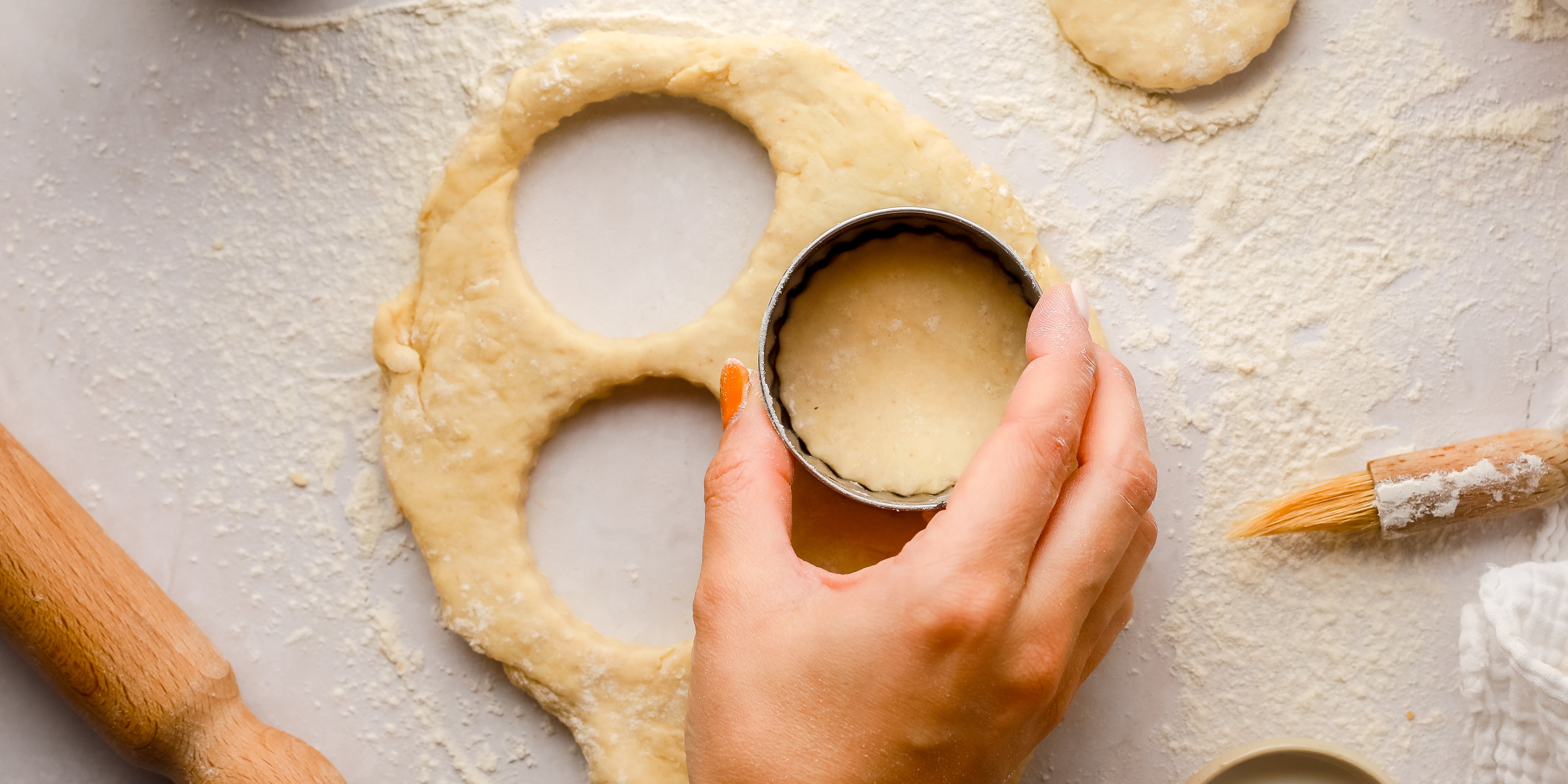 Hand using stencil to cut scone shape in dough with flour with brush in the background