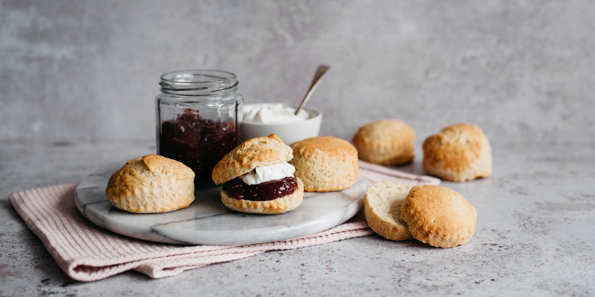 Vegan Scones served on a marble board, cut in half and smothered in jam and plant based cream