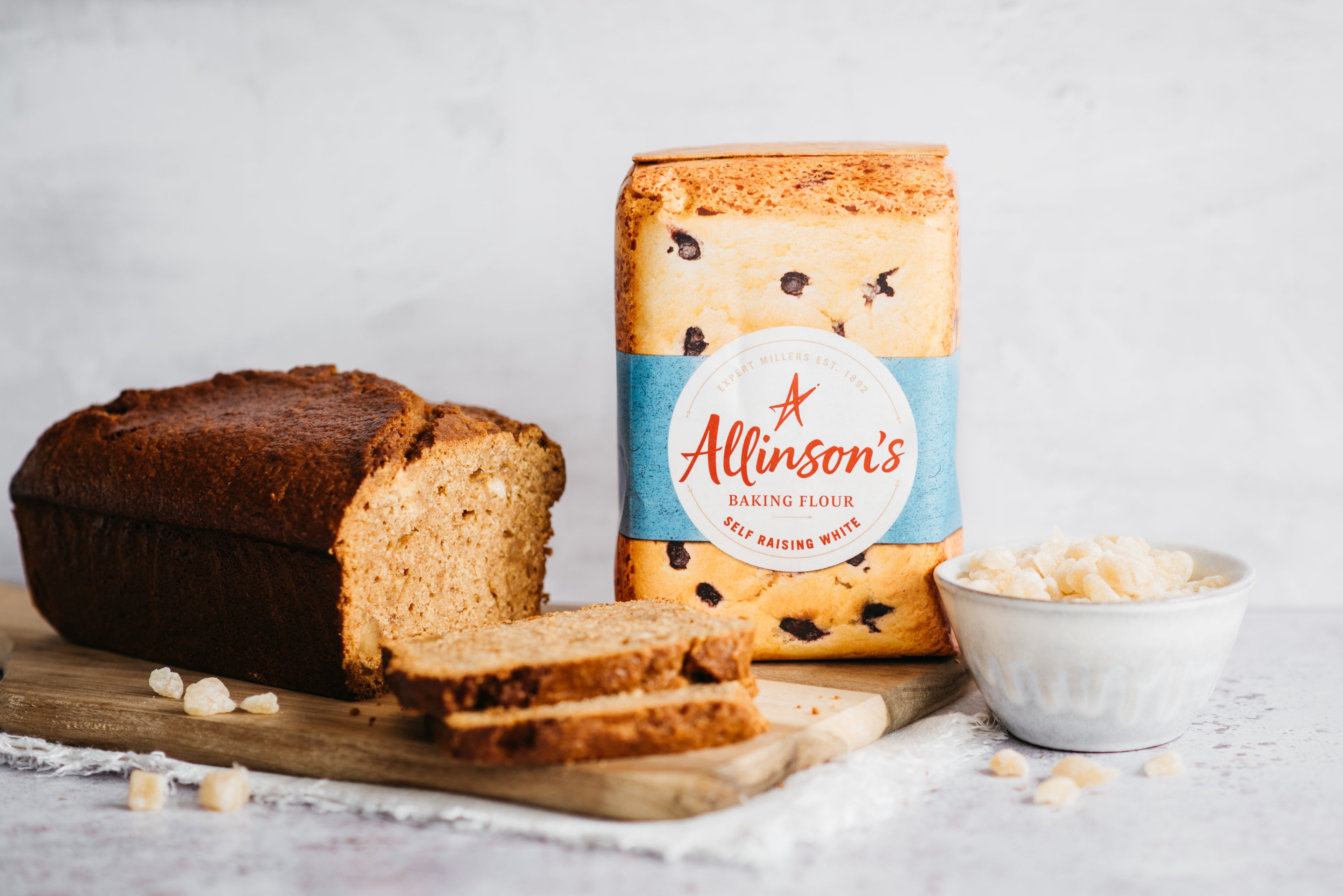 Gingerbread Loaf on a wooden serving board, with a bag of Allinson's self raising flour in the background