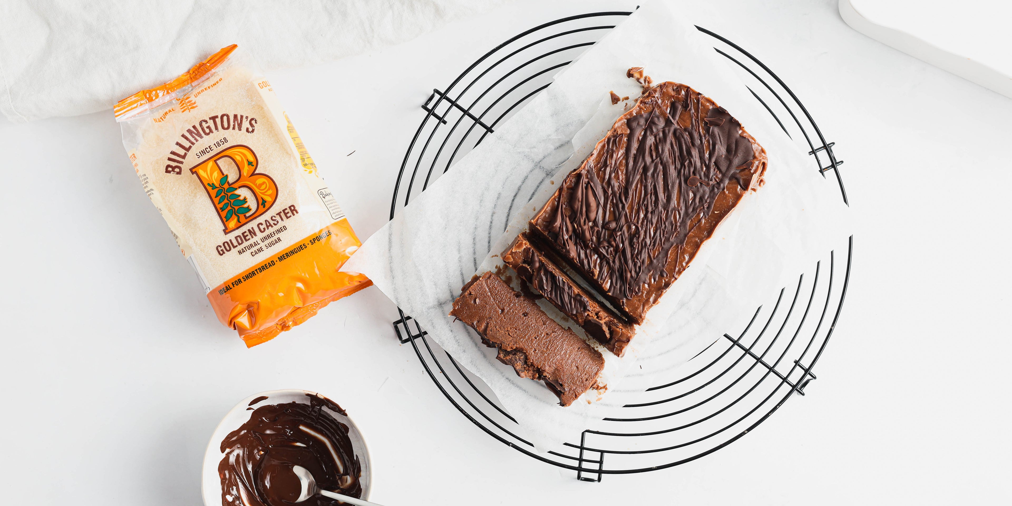 Top down view of a sliced chocolate halva next to a bag of Billington's golden caster sugar