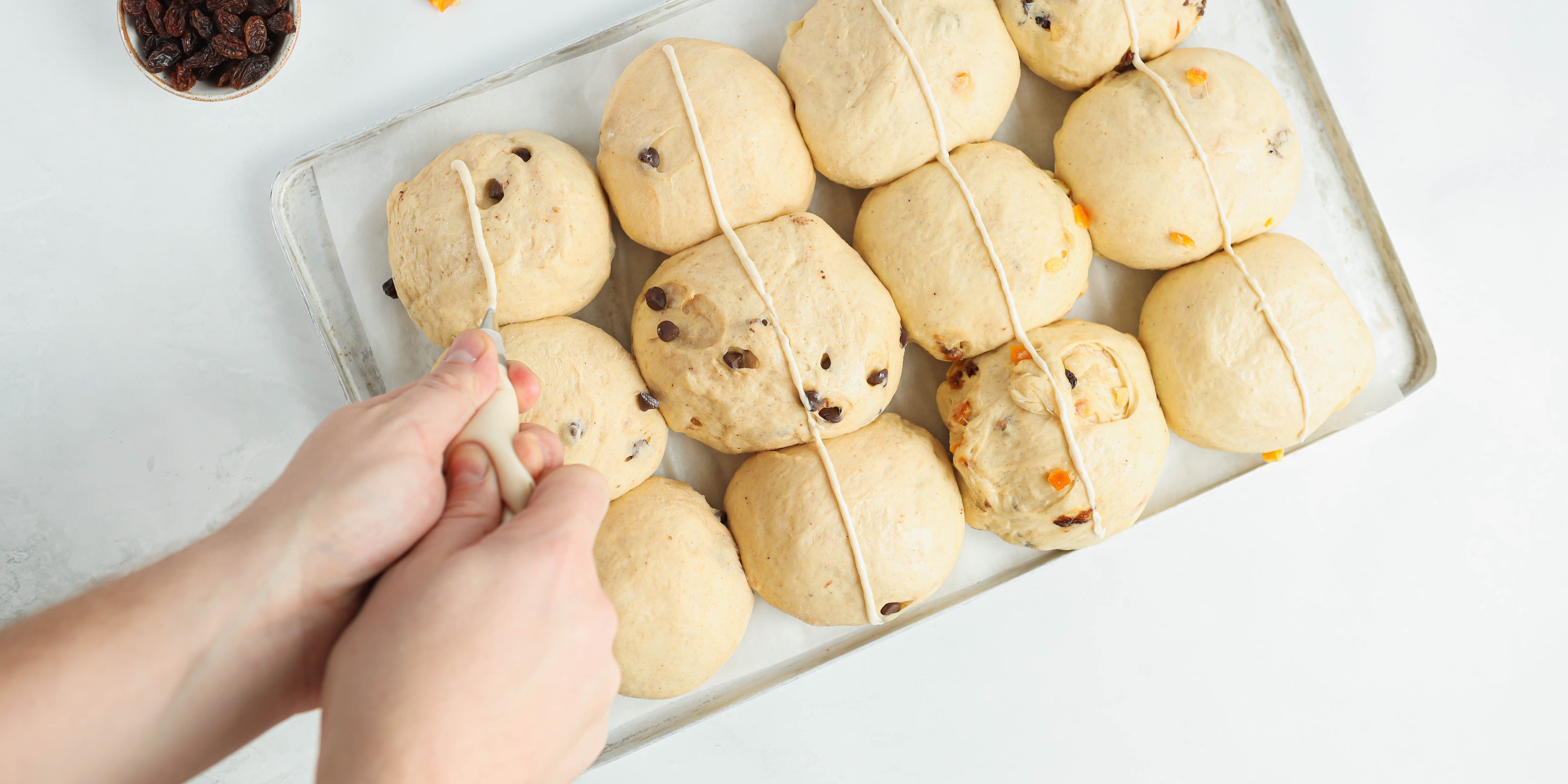 Vegan Hot Cross Buns being piped with a hand holding a piping bag, ready to bake in the oven