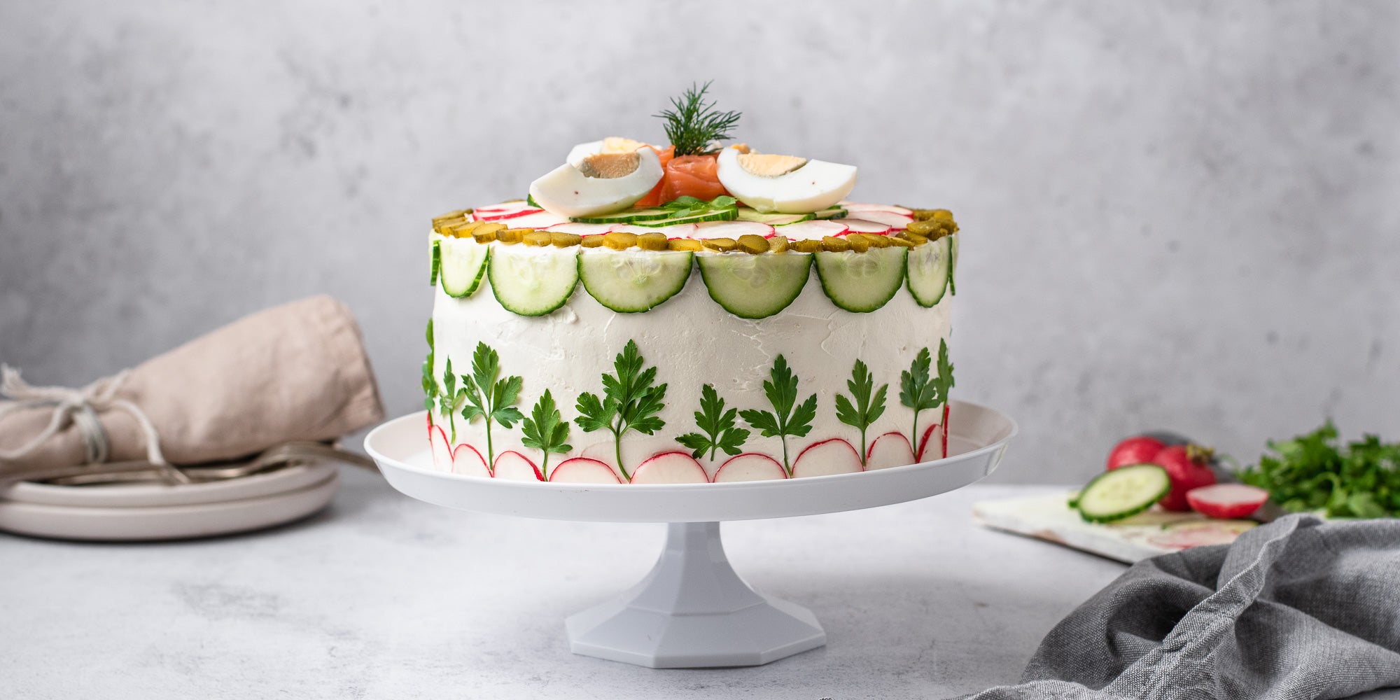 Smörgåstårta Sandwich Cake on a white cake stand with napkins and white plates in background