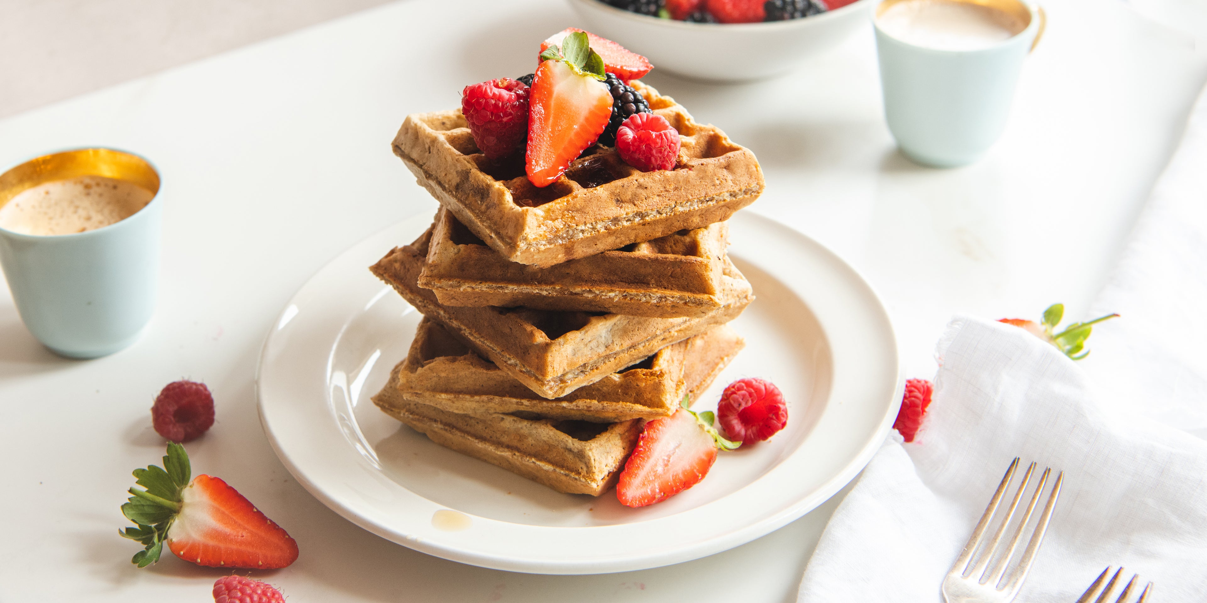 Wholemeal Banana Waffles topped with strawberries next to a coffee