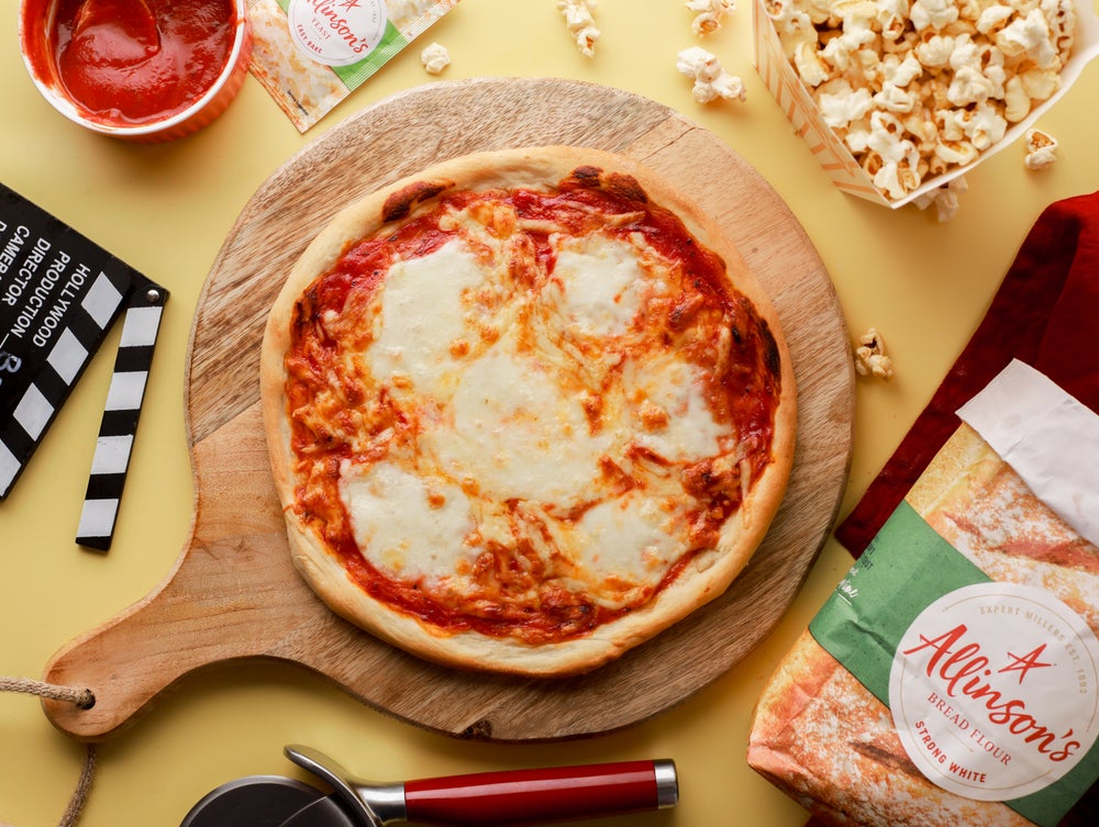 Homemade pizza on a circular wooden board next to some popcorn