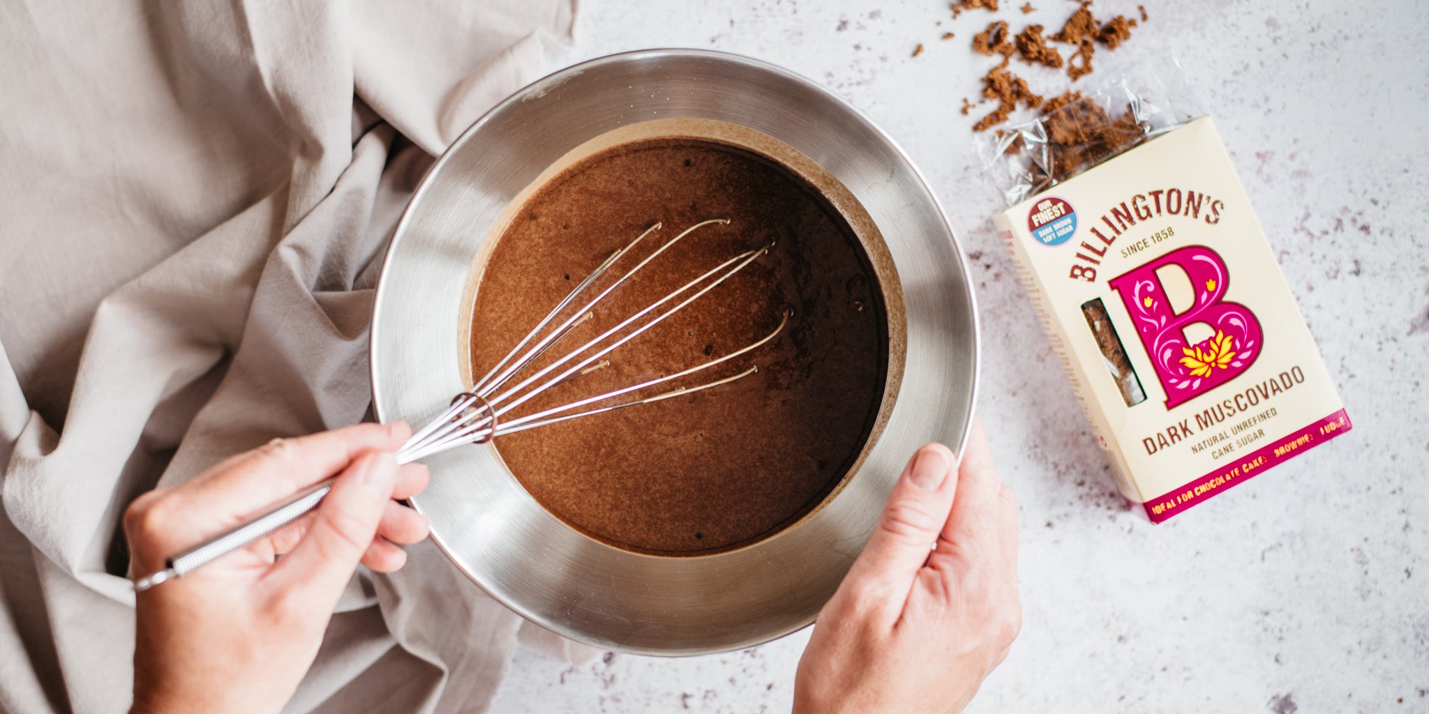 Chocolate batter in bowl with whisk and open sugar packet beside it