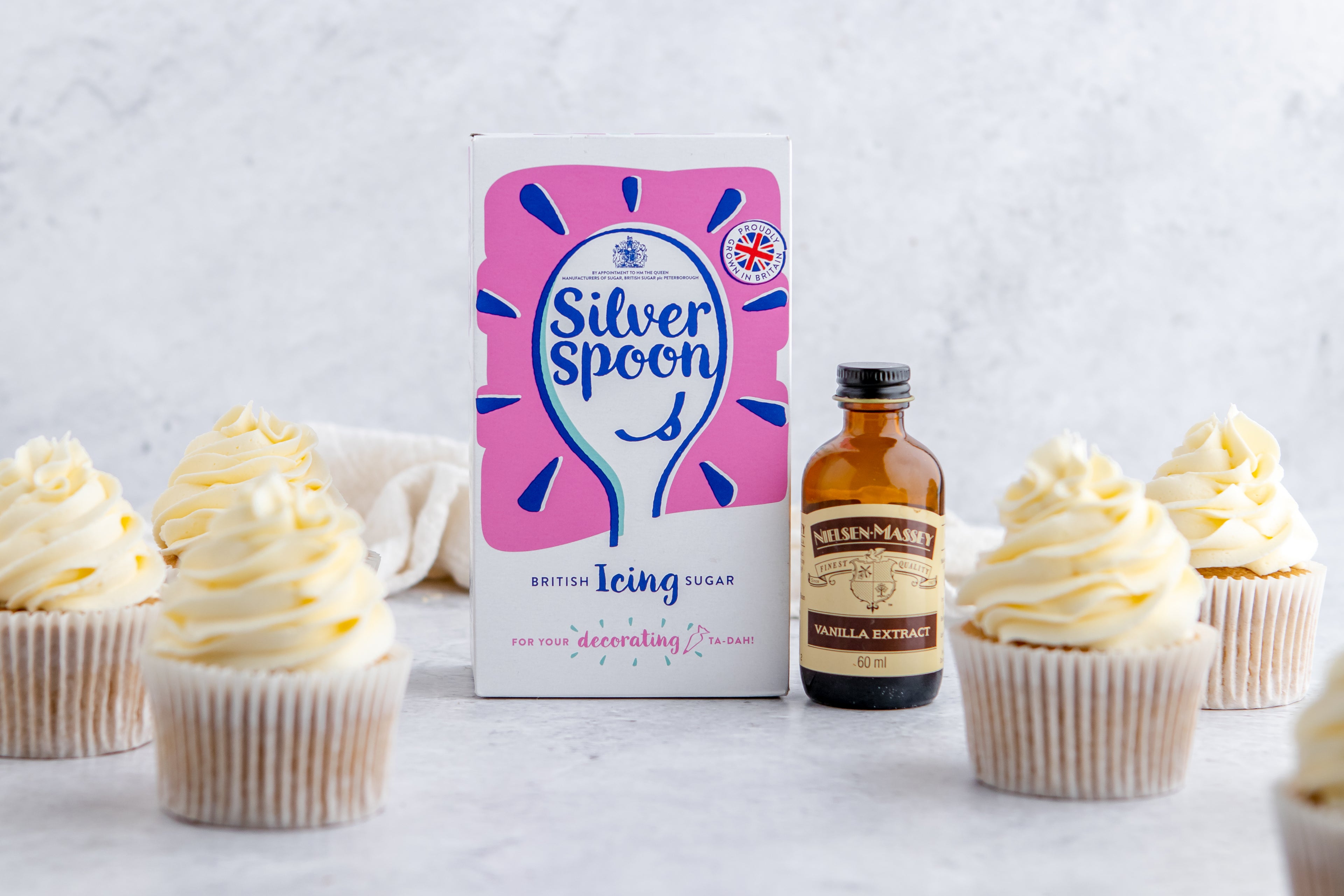 Silver Spoon Icing sugar and Neilsen-Massey vanilla extract surrounded by Gluten Free Cupcakes