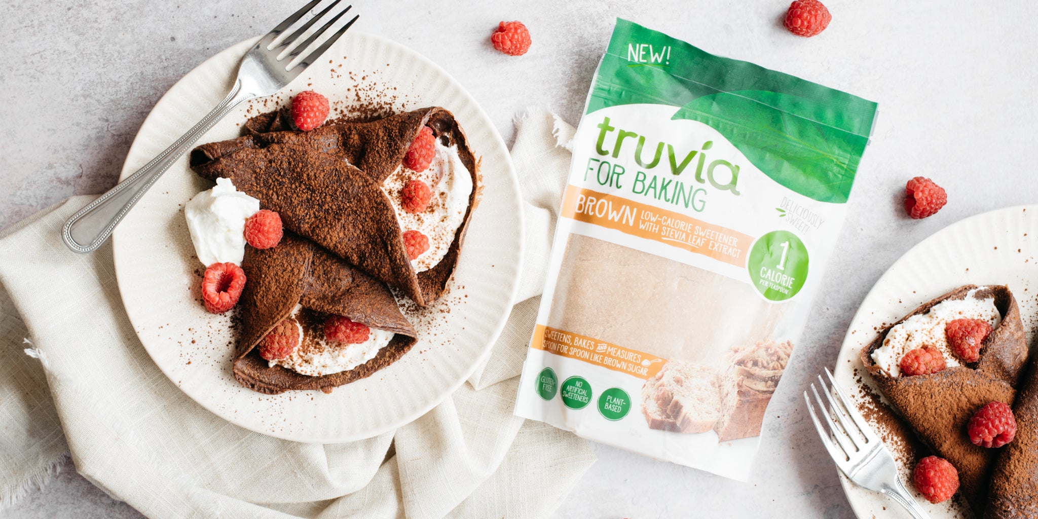 White plate with two chocolate crepes filled with cream and raspberries. Beside the plate is a pack of Truvia brown sweetener