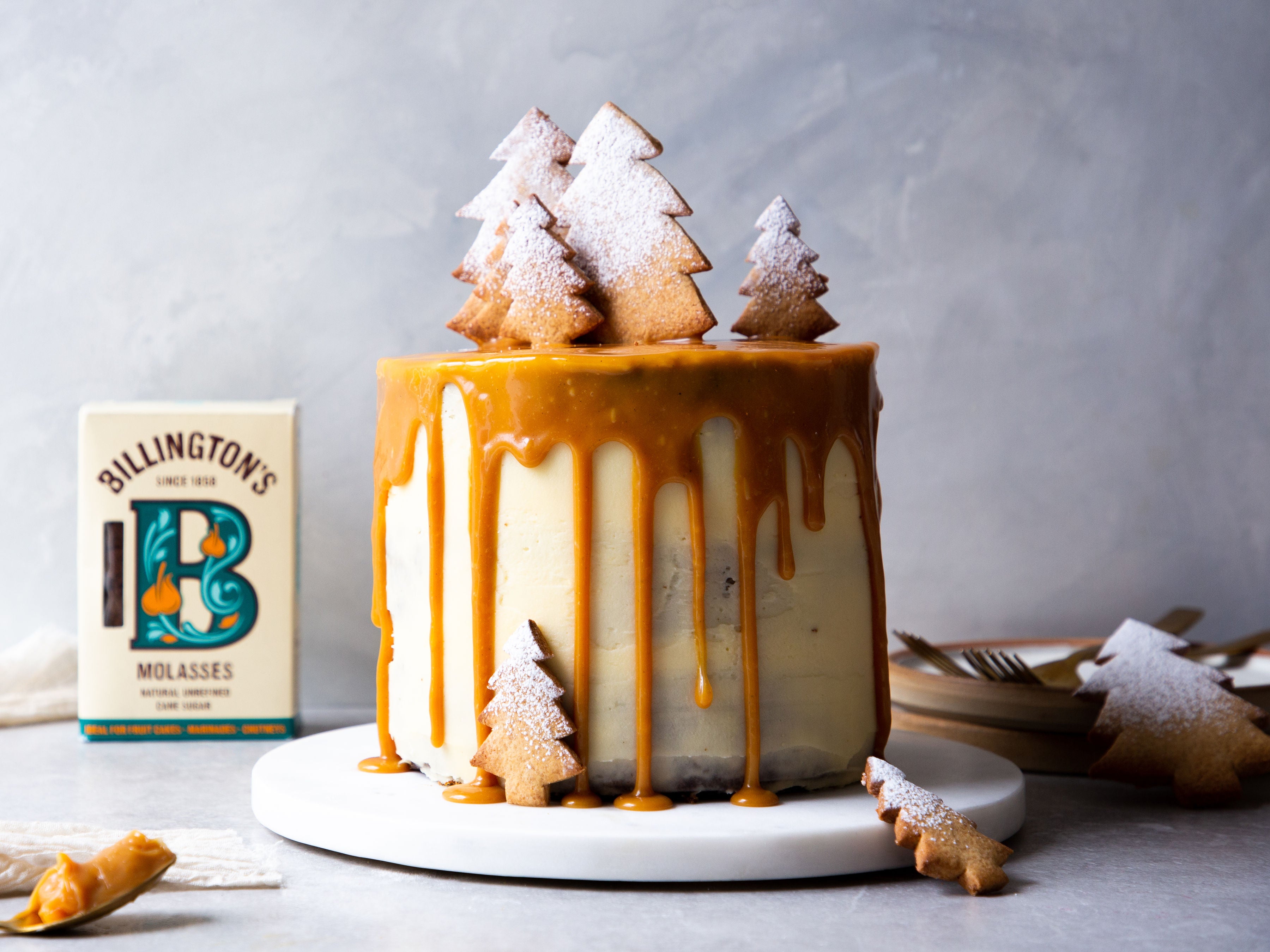 Gingerbread Birthday Cake topped with gingerbread Christmas trees dusted in icing sugar, with a box of Billington's Molasses in the background.