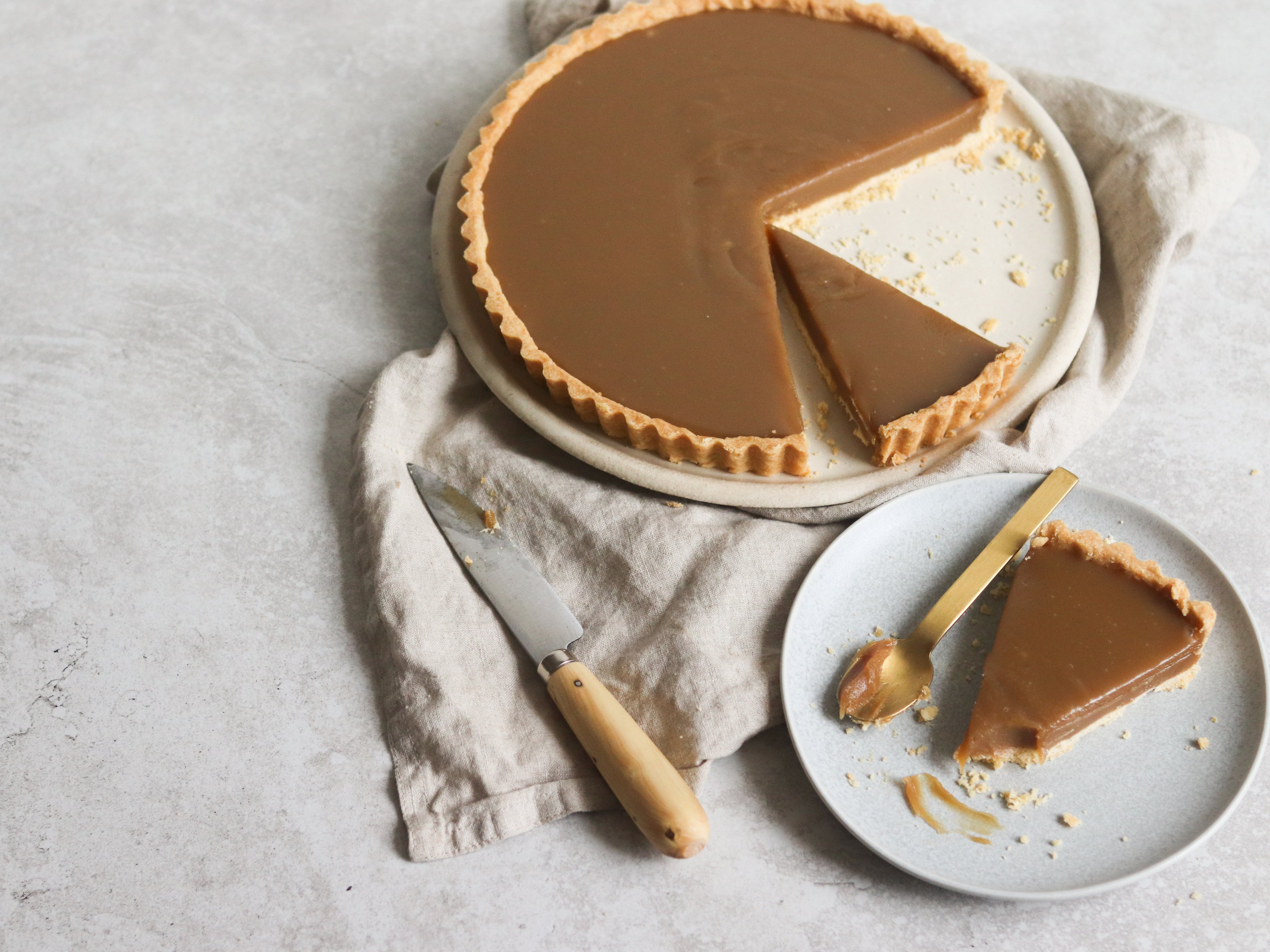 Butterscotch Tart top view, with a slice cut out of it, on a plate with a spoonful of butterscotch