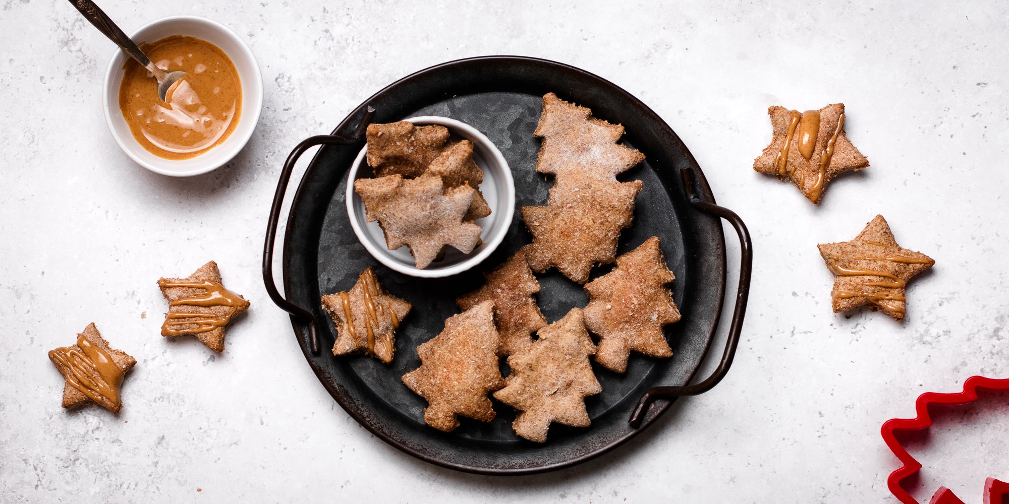 Dog Biscuits cut into festive shapes on a black serving tray next to a bowl of Proper Nutty peanut butter