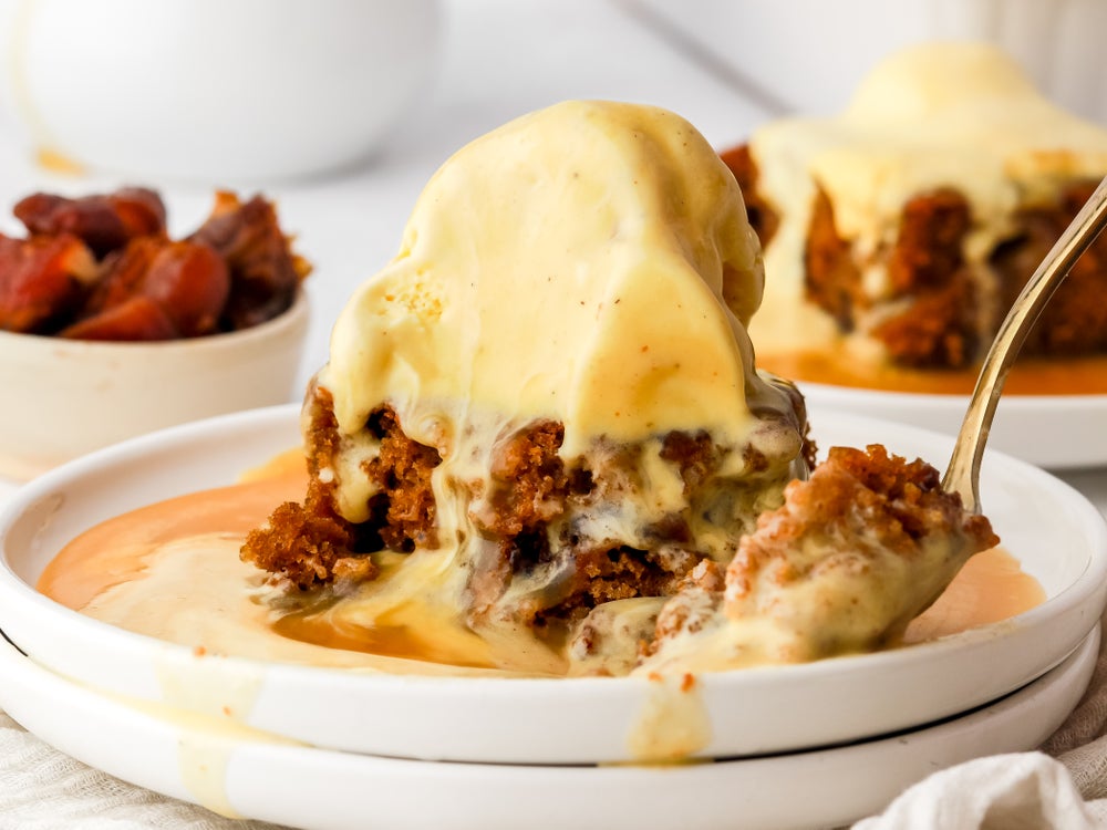 Close up of a sticky toffee pudding with melted ice cream on top and spoonful taken out