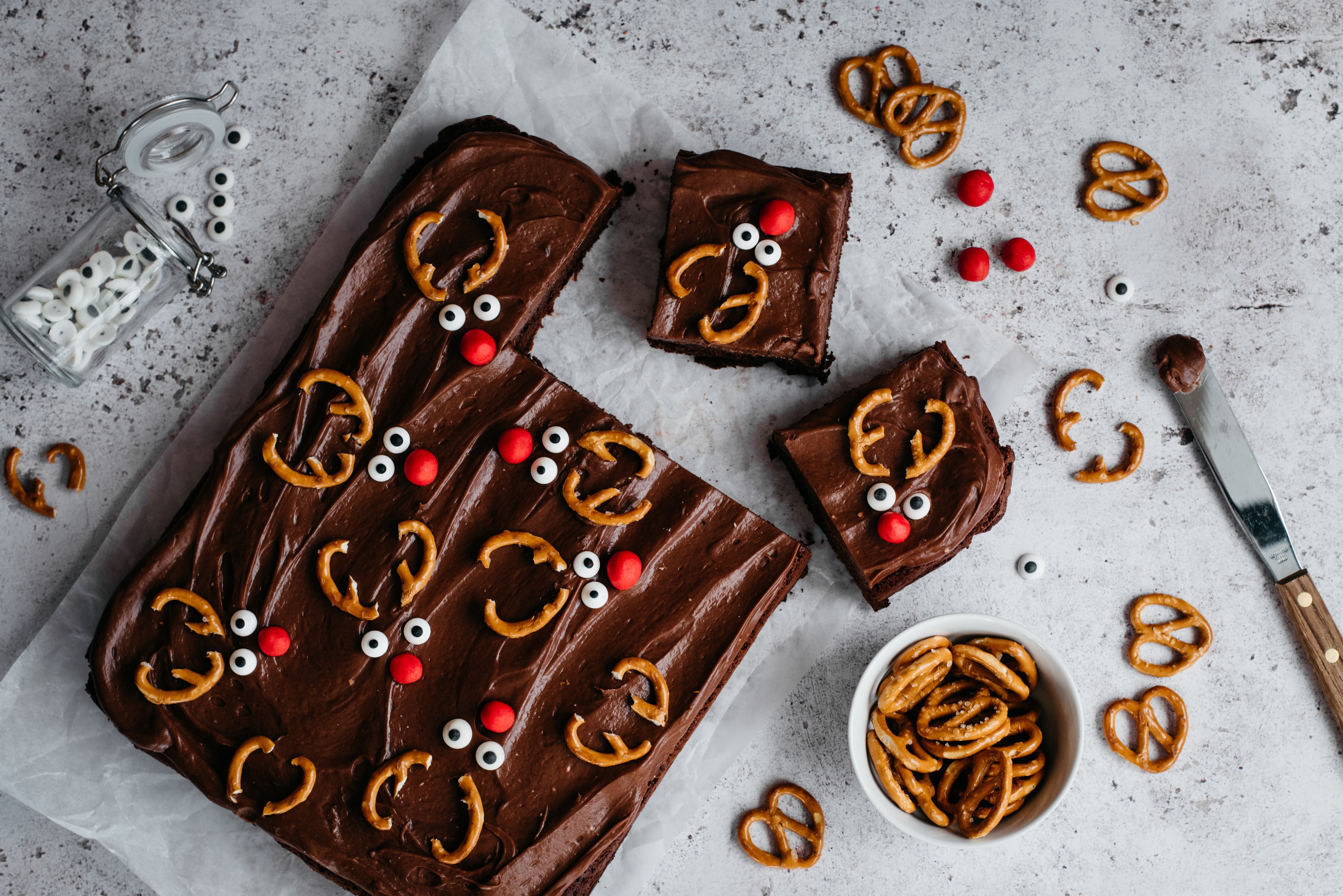 Chocolate & Caramel Reindeer Traybake with slices cut out, decorated with pretzels and red sweets.