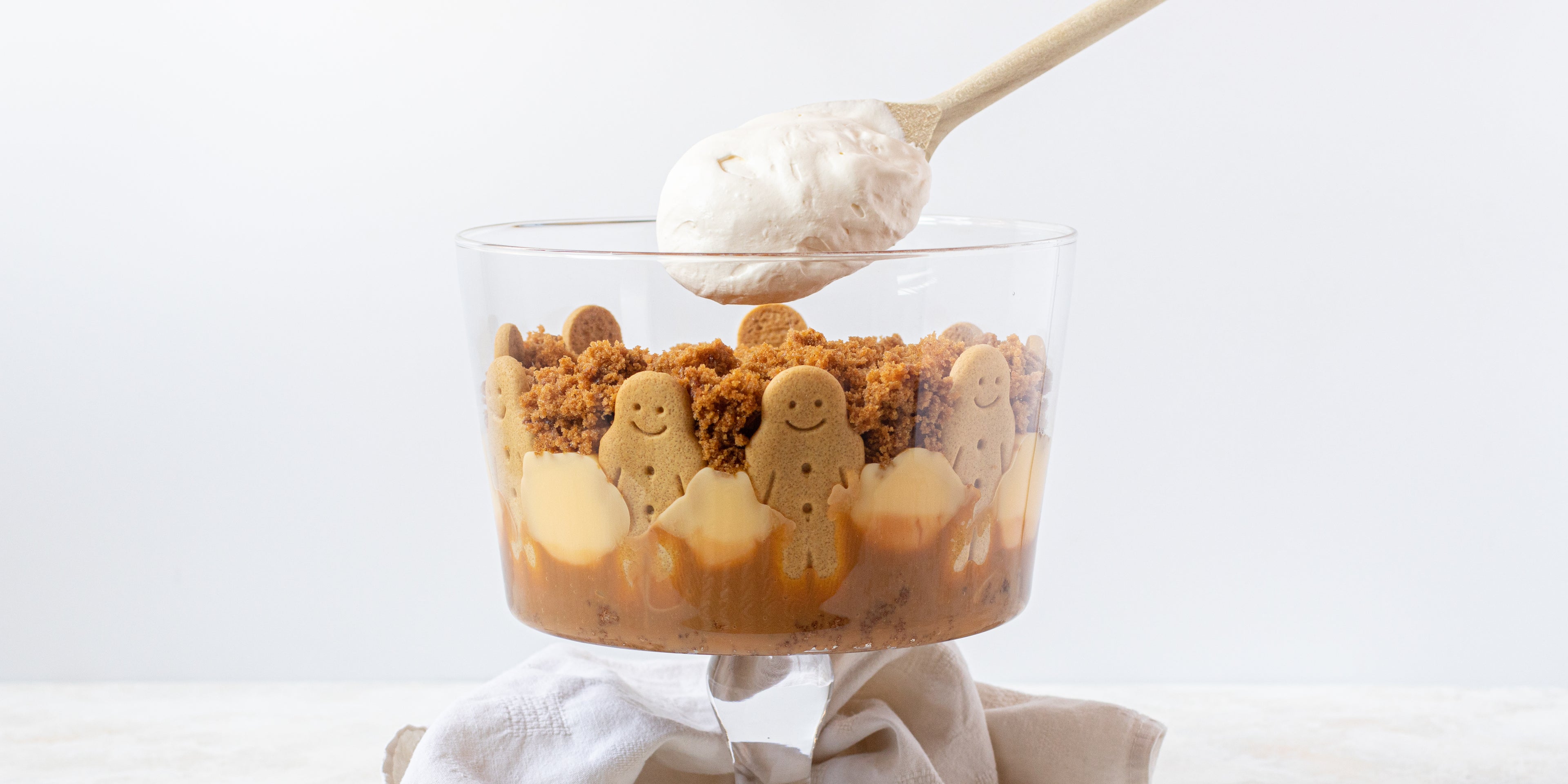 Gingerbread Trifle with a wooden spoon layering the trifle with a dollop of cream